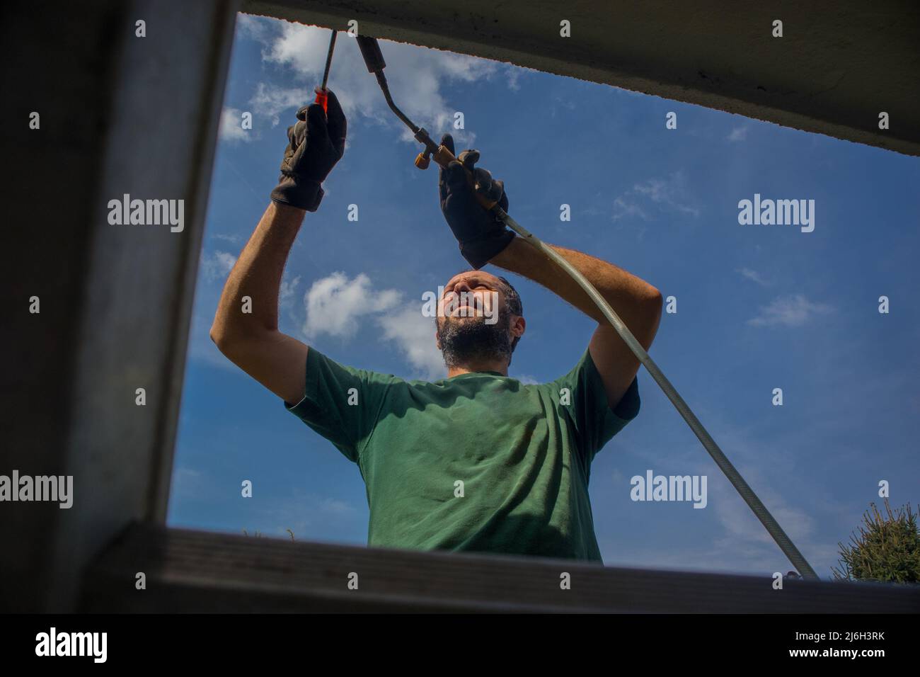 L'uomo utilizza una torcia termica o una pistola termica per applicare l'isolamento bituminoso sul bordo di un tetto o l'isolamento dell'acqua sul bordo di calcestruzzo di una casa utilizzando una scala Foto Stock