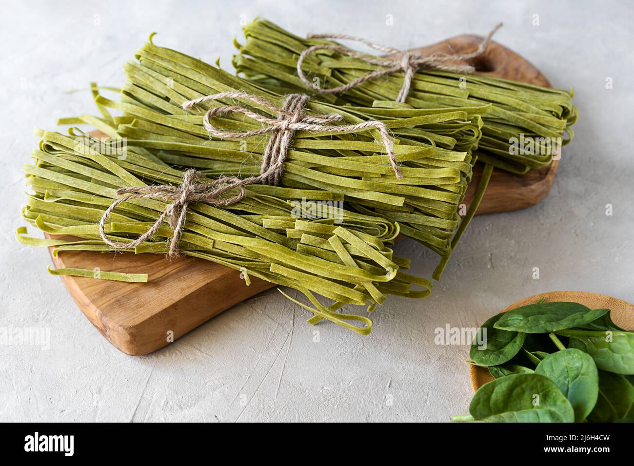 Fasci di fettuccine di pasta cruda con spinaci su tagliere in legno e fondo in calcestruzzo Foto Stock
