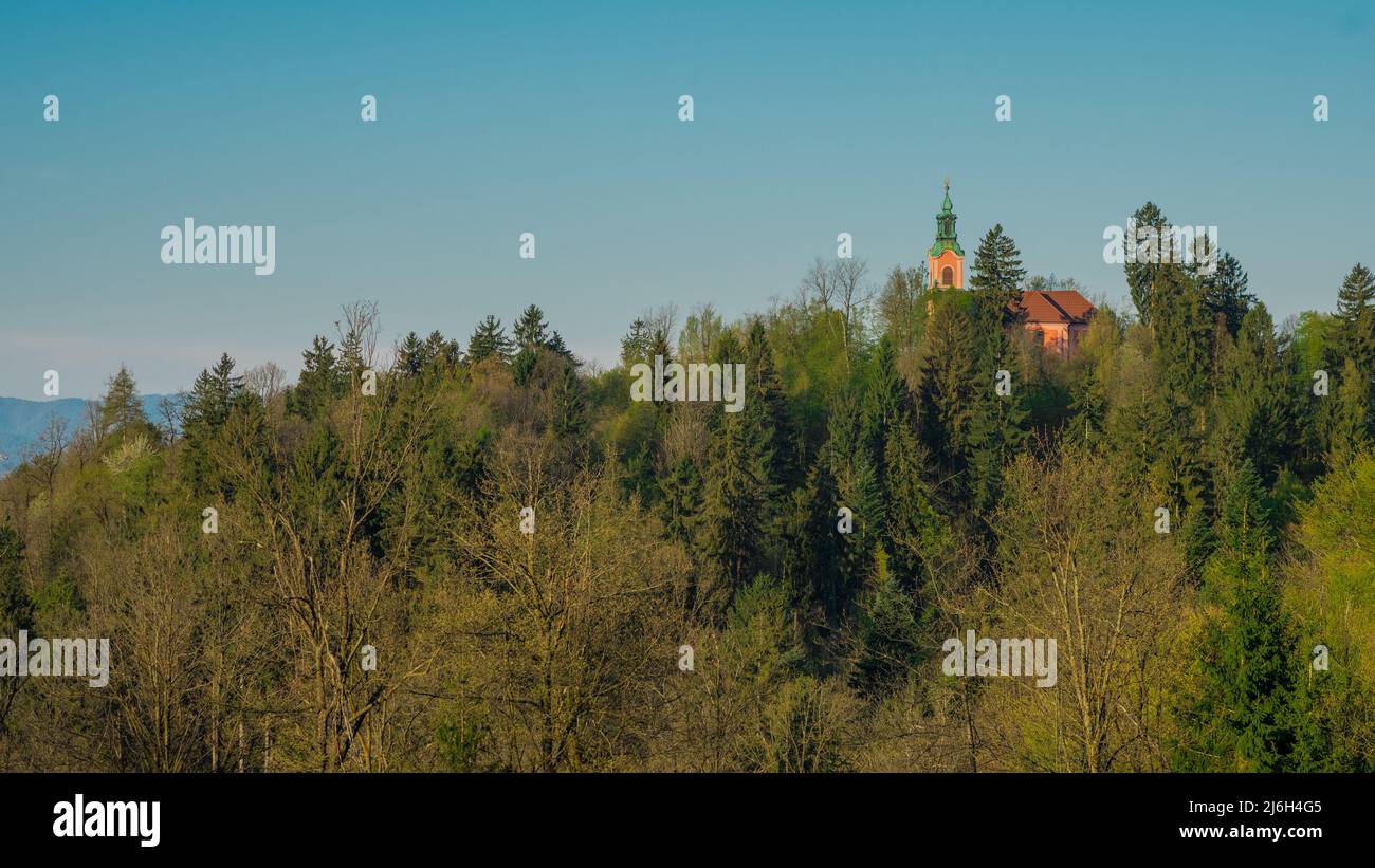 Panorama della collina di Roznik con chiesetta rossa che si nasconde dietro gli alberi al sole di prima mattina. Foto Stock