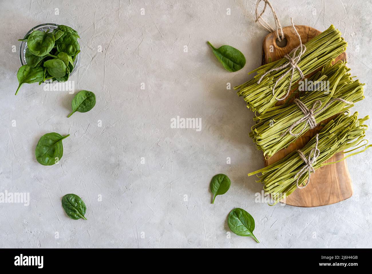 Fasci di fettuccine di pasta cruda con spinaci su tagliere in legno e fondo in calcestruzzo Foto Stock