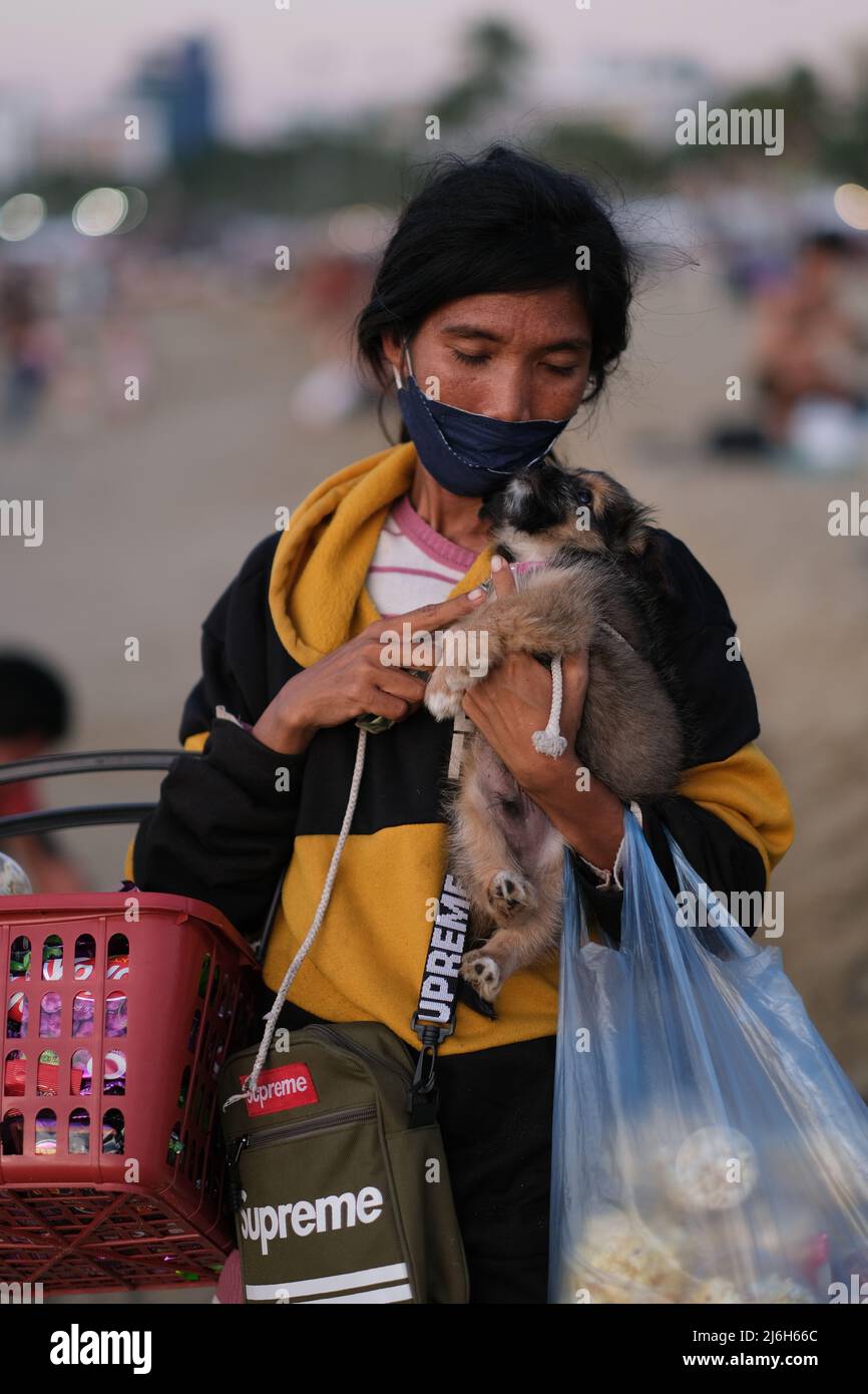 Pattaya, Chonburi Thailandia - Dicembre 11 2021: Povera donna asiatica sta tenendo un cucciolo mentre vende spuntini sulla spiaggia Foto Stock