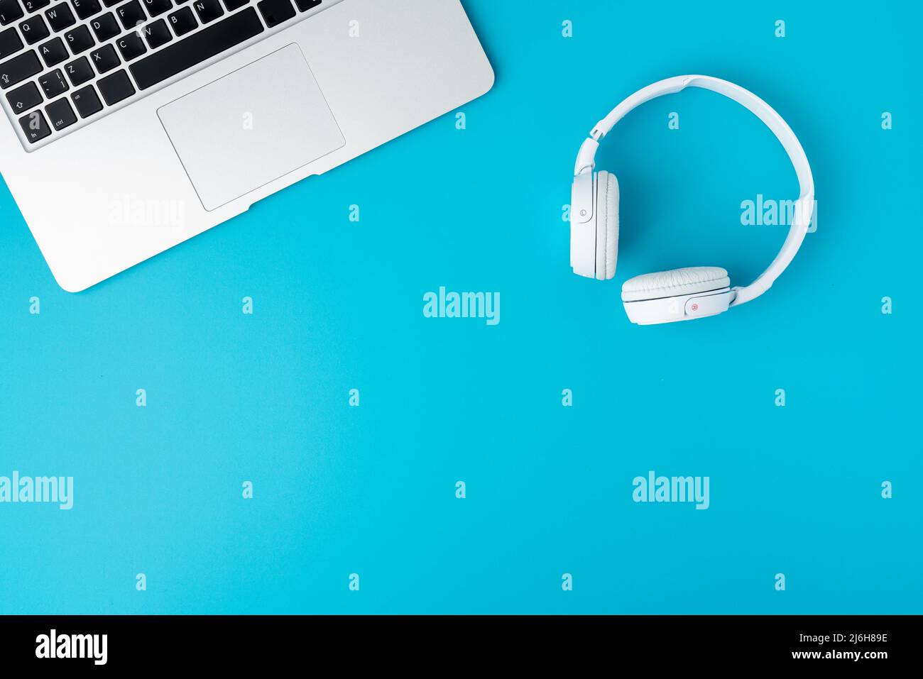Design piatto di cuffie digitali bianche e laptop con tastiera ritagliata su sfondo blu Foto Stock