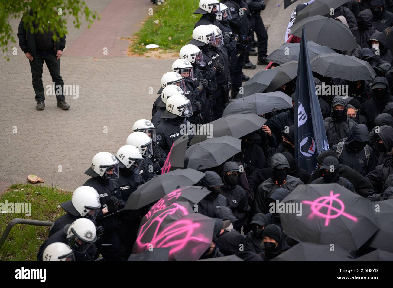 01 maggio 2022, Amburgo: Partecipanti alla manifestazione sotto il motto 'verboten gut - Anarchismo in die offensive - Anarchistischer 1. Mai' stand in un circondamento di polizia. Poco dopo l'inizio, la polizia ha bloccato la processione per la prima volta, come pirotecnica sono stati accesi, molti dimostranti sono stati agganciati e volevano marciare sotto un tetto di ombrelloni neri, coperto da striscioni. Senza ombrelloni, la processione è stata finalmente lasciata iniziare dopo poco meno di tre quarti d'ora. Foto: Jonas Walzberg/dpa Foto Stock