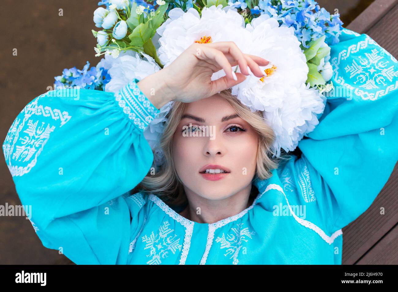Bella giovane donna Ucraina vestita in un abito blu ricamato con una grande bella corona floreale sulla testa tiene un fiore secco nelle sue mani Foto Stock