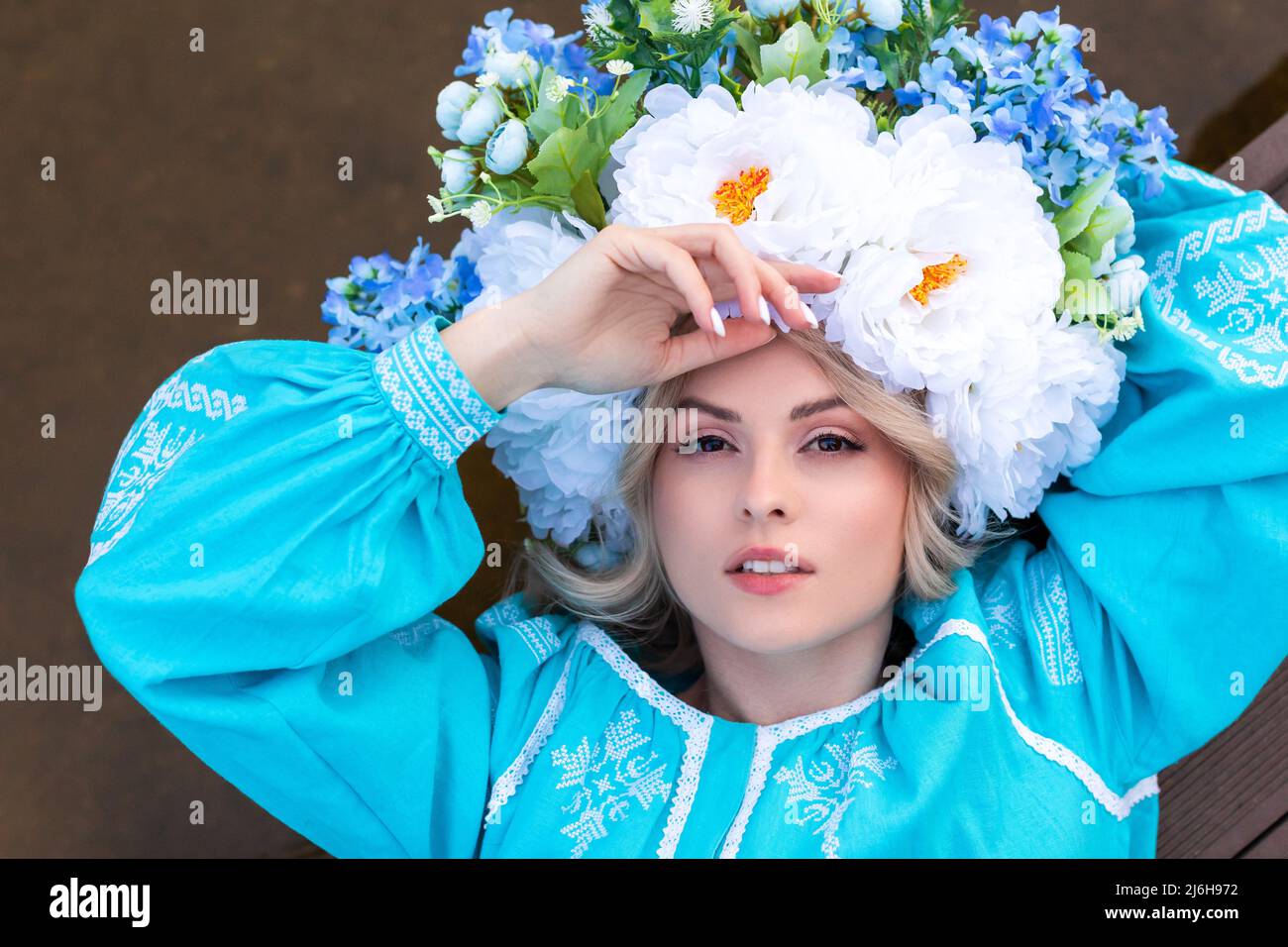 Bella giovane donna Ucraina vestita in un abito blu ricamato con una grande bella corona floreale sulla testa tiene un fiore secco nelle sue mani Foto Stock