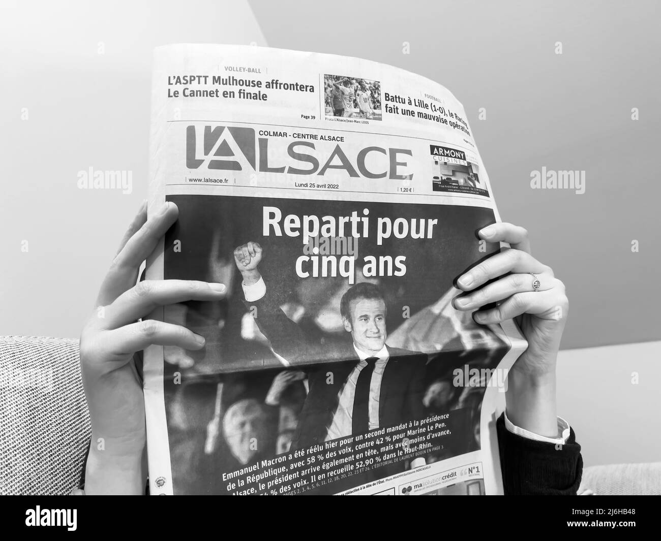 Parigi, Francia - 25 apr 2022: Donna che legge su un divano accogliente ultimo giornale francese l'Alsace, coprire con la Francia presidente in carica Emmanuel Macron dopo aver battuto Marine le Pen per un secondo quinquennio Foto Stock