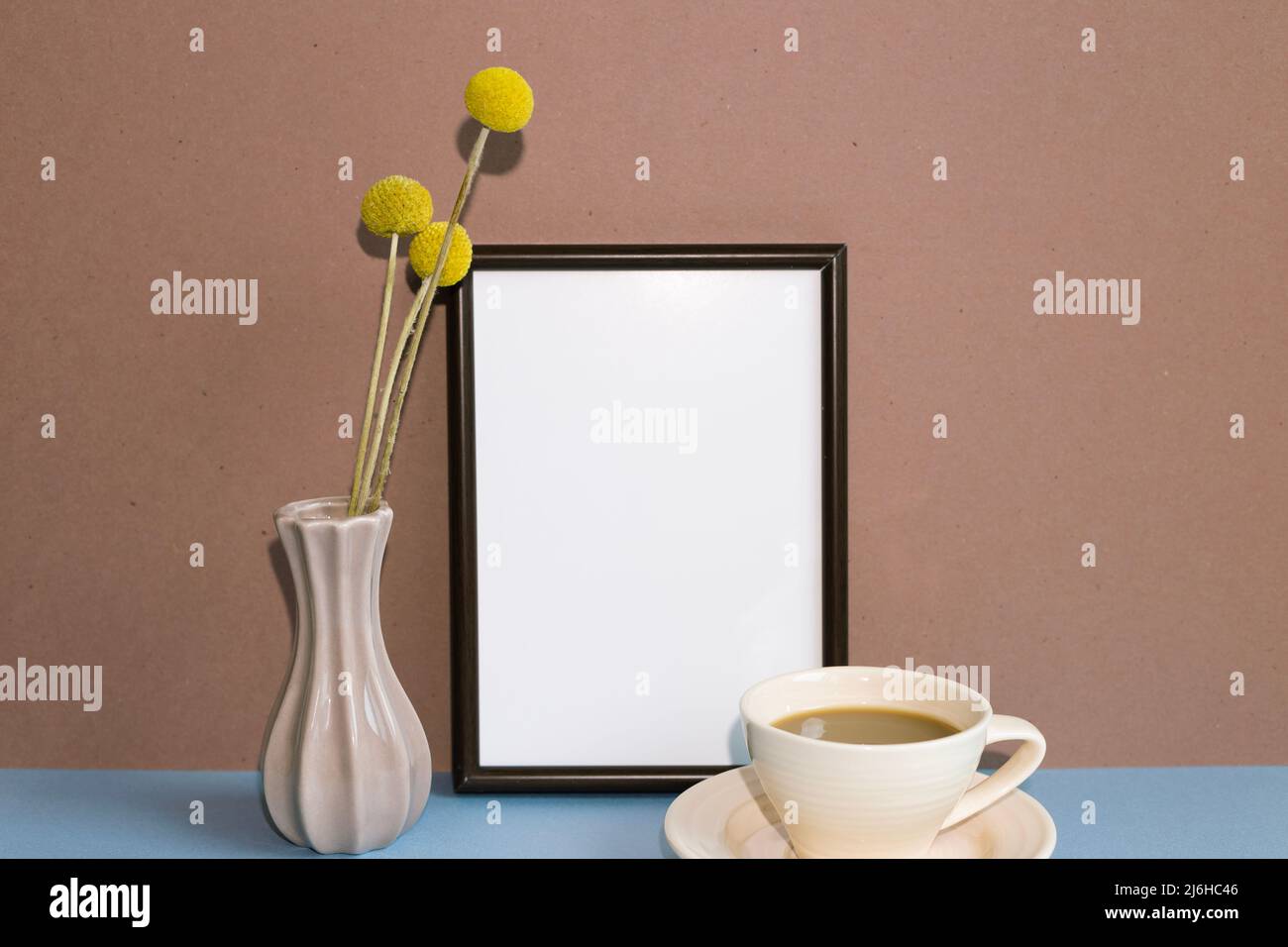 Cornice bianca con fiore secco e tazza di caffè su un tavolo blu. Sfondo marrone. Spazio copia Foto Stock