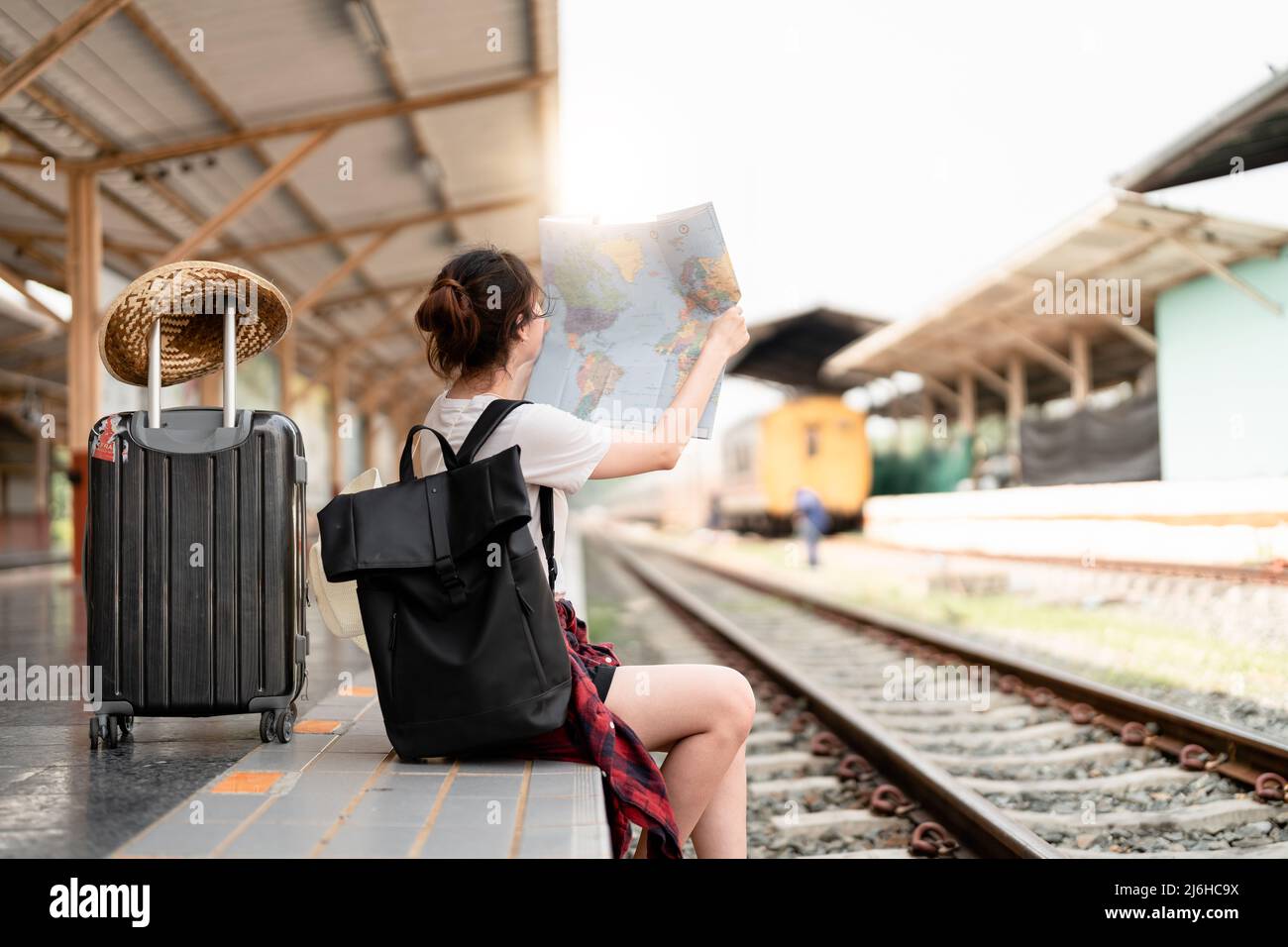 Giovane donna viaggiatore con zaino in cerca di mappa in attesa di treno, saccopelatore asiatico sulla piattaforma ferroviaria alla stazione ferroviaria. Vacanza, viaggio Foto Stock