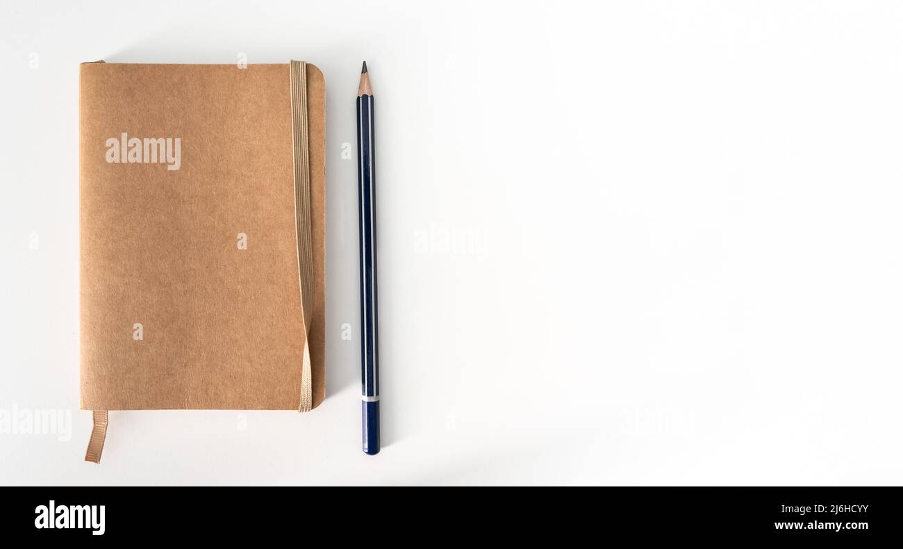 vista dall'alto di un piccolo notebook marrone e di una matita appuntita sulla scrivania bianca Foto Stock
