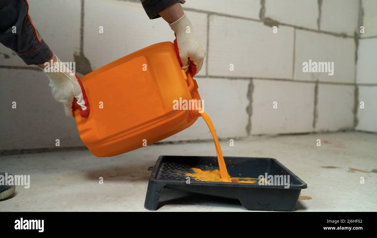Il primer arancione viene versato dal contenitore. Primer arancione. Tanica, rullo e vassoio di vernice arancione. Foto Stock