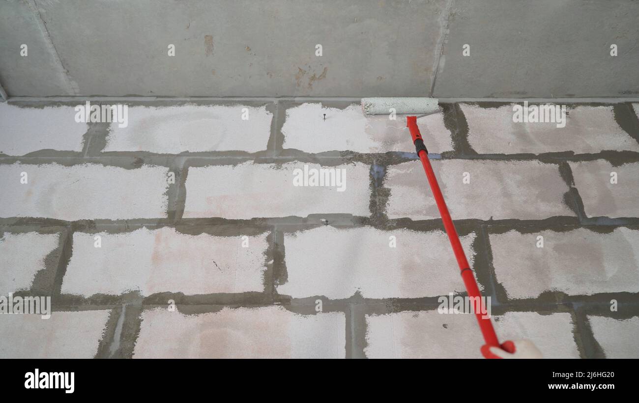 Applicazione di un primer su una parete del blocco. Applicazione a rullo del sigillante impermeabilizzante alla parete. Foto Stock