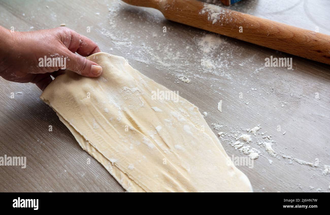 Impastare l'impasto. Rullo di pasta e farina maschio su un tavolo da cucina, vista ravvicinata. Fare torta o pasticceria su legno Foto Stock