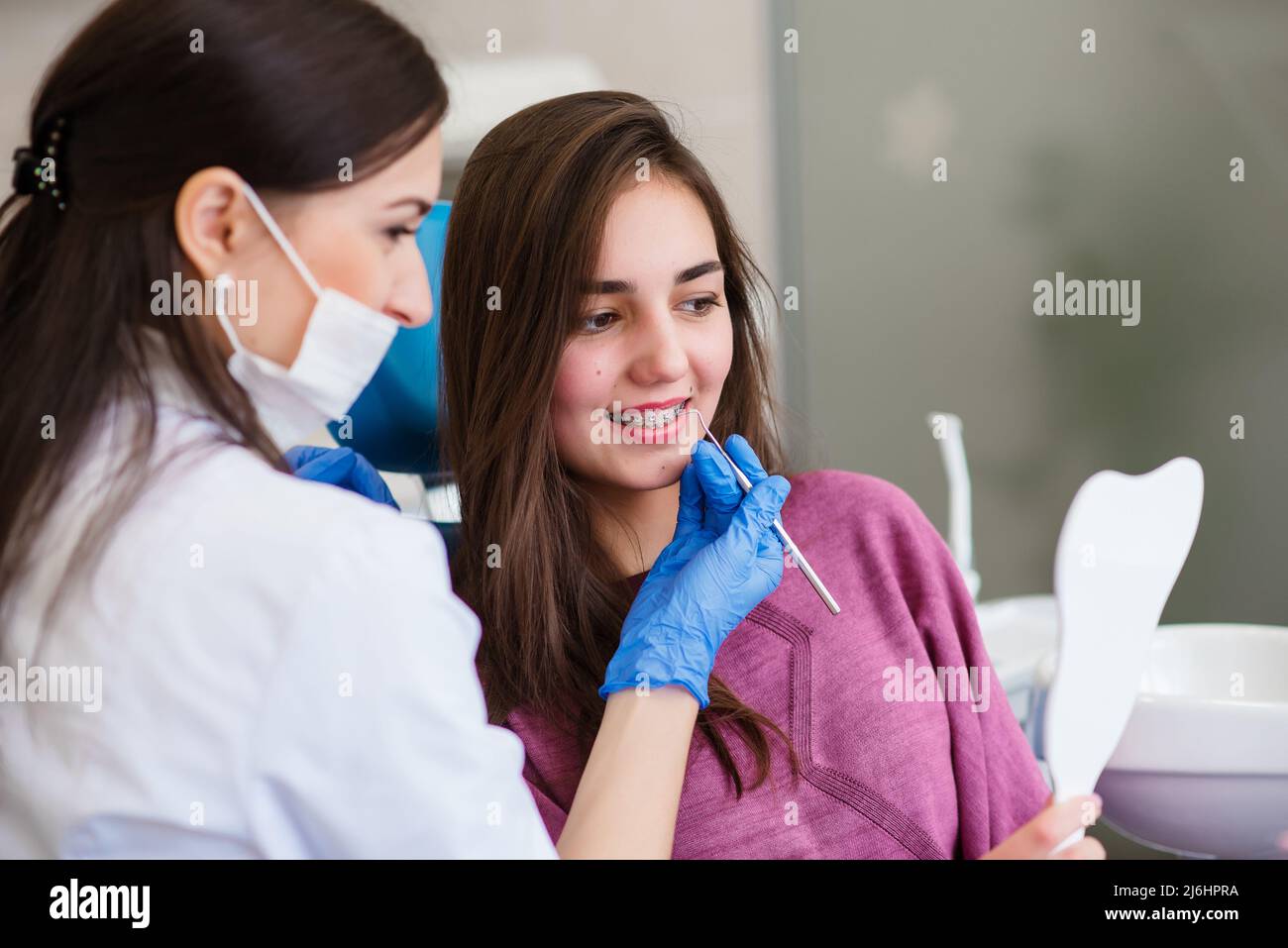 Sorridendo ragazza giovane sta cercando nello specchio per stimare il lavoro del dentista e godendo del risultato con lo specialista. Foto Stock