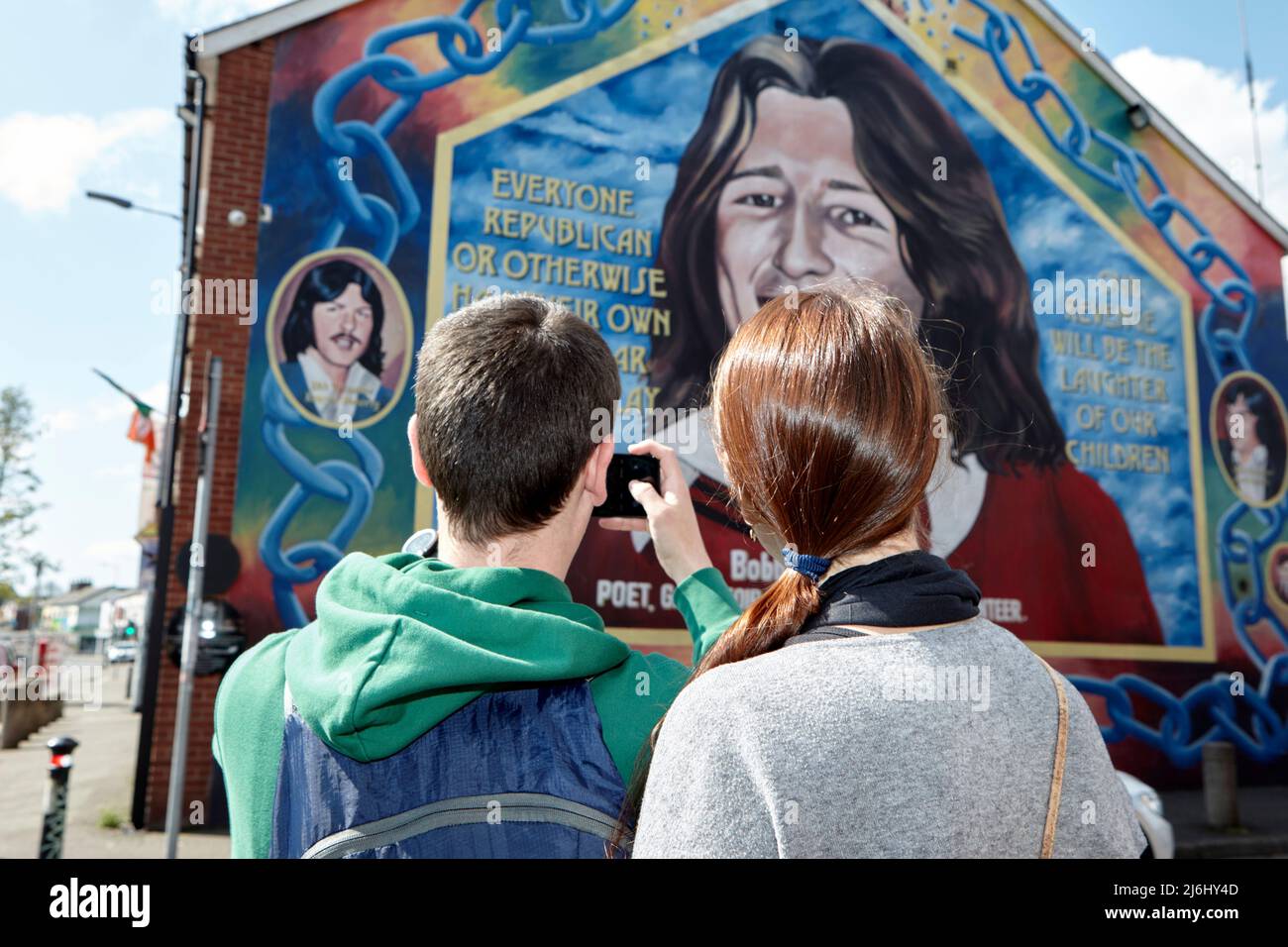 Coppia di turisti dalla Spagna scattare foto al murale di Bobby Sands sulla parete dell'ufficio del Sinn Fein, Lower Falls Road, West Belfast, Irlanda del Nord, Foto Stock
