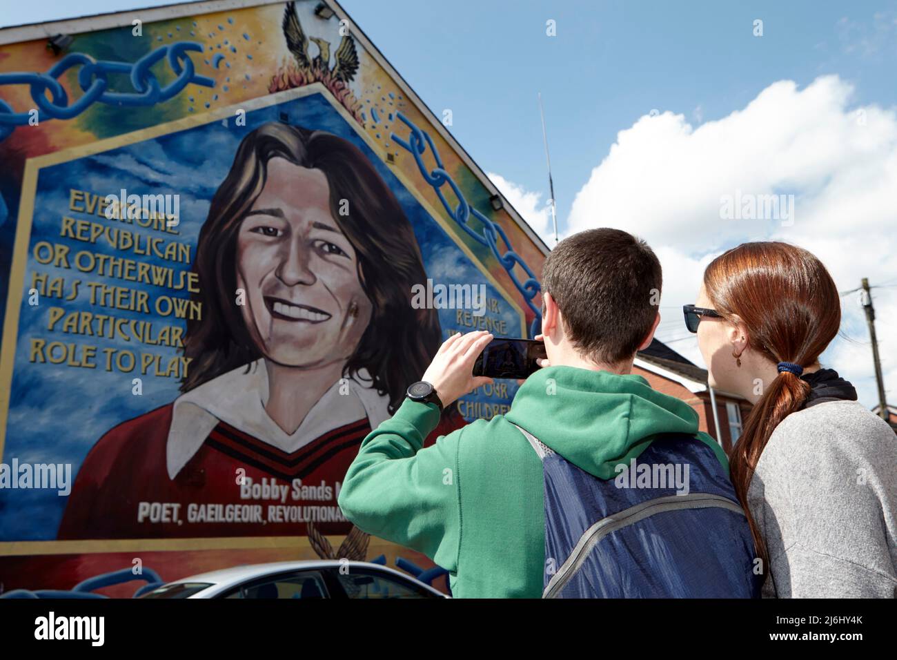 Coppia di turisti dalla Spagna scattare foto al murale di Bobby Sands sulla parete dell'ufficio del Sinn Fein, Lower Falls Road, West Belfast, Irlanda del Nord, Foto Stock