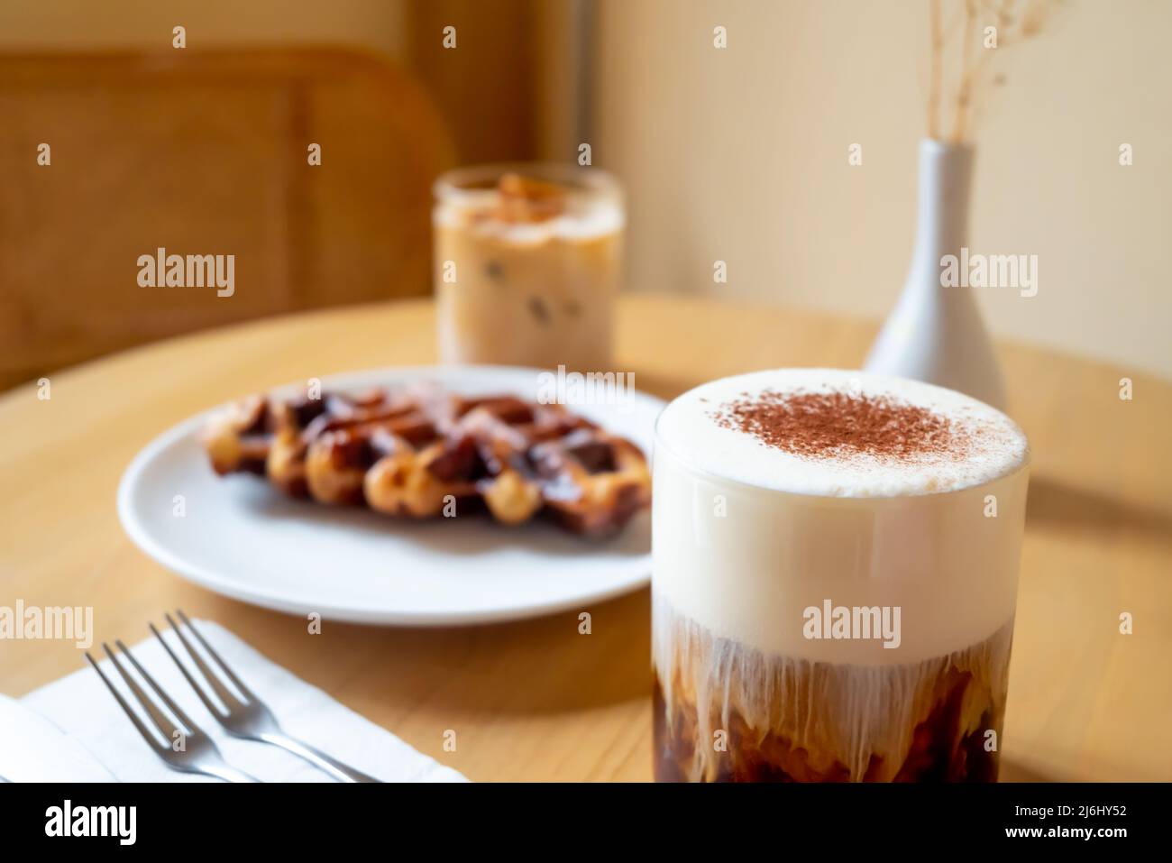 Un pasto di domenica mattina in caffetteria, due tazze di caffè, latte di miele e Eispanner americano servito con waffle sul piatto, decorato con vaso. Foto Stock