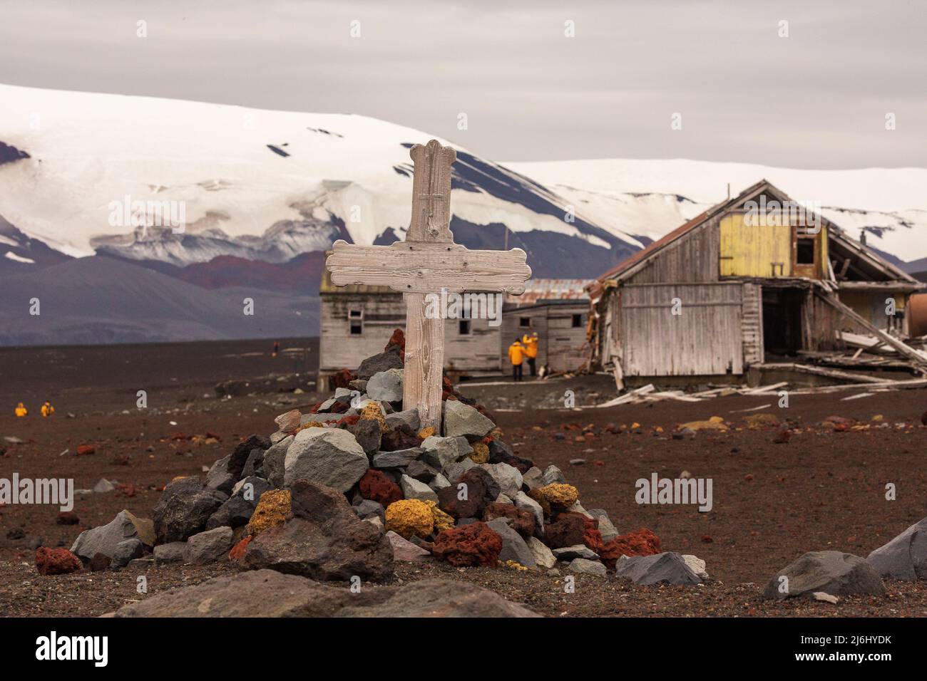 una semplice croce di legno su un piccolo carirno roccioso si erge di fronte a montagne innevate e edifici fatiscenti dell'isola inganno antartide Foto Stock