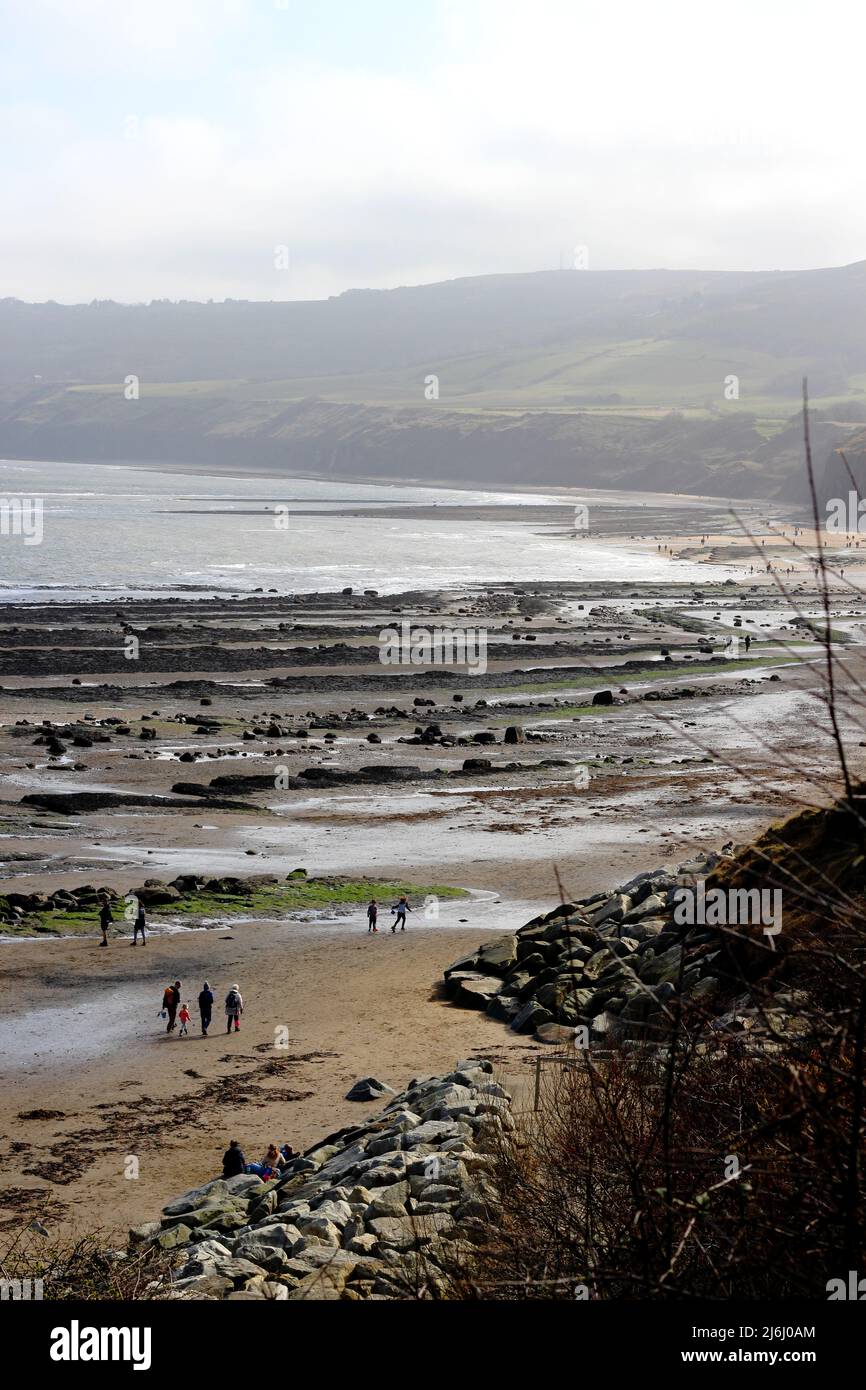 Famiglie che camminano tra le piscine di roccia e il mare scintillante di Robin Hood's Bay, Yorkshire, Regno Unito Foto Stock