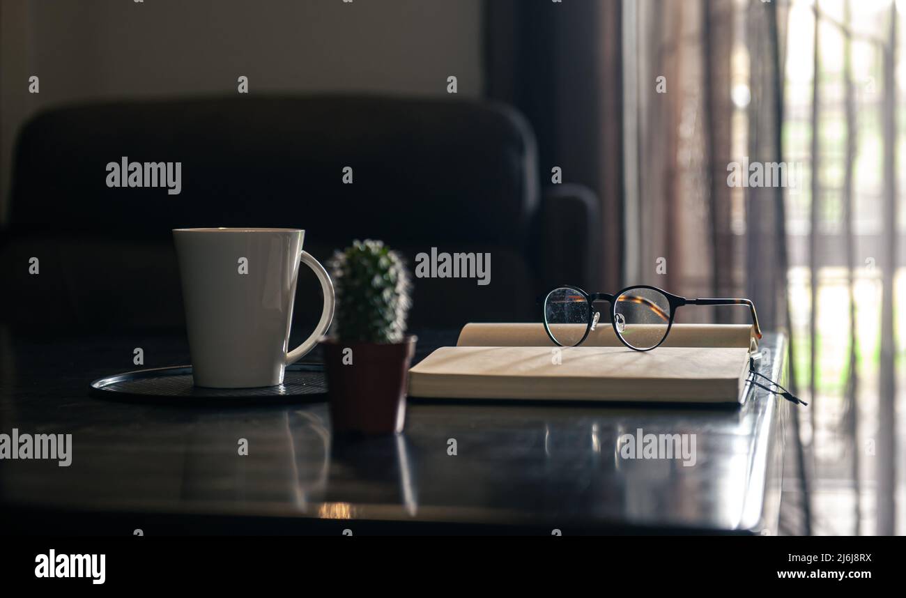 Aprire il notebook, la tazza e gli occhiali sul tavolo, sfondo sfocato. Foto Stock