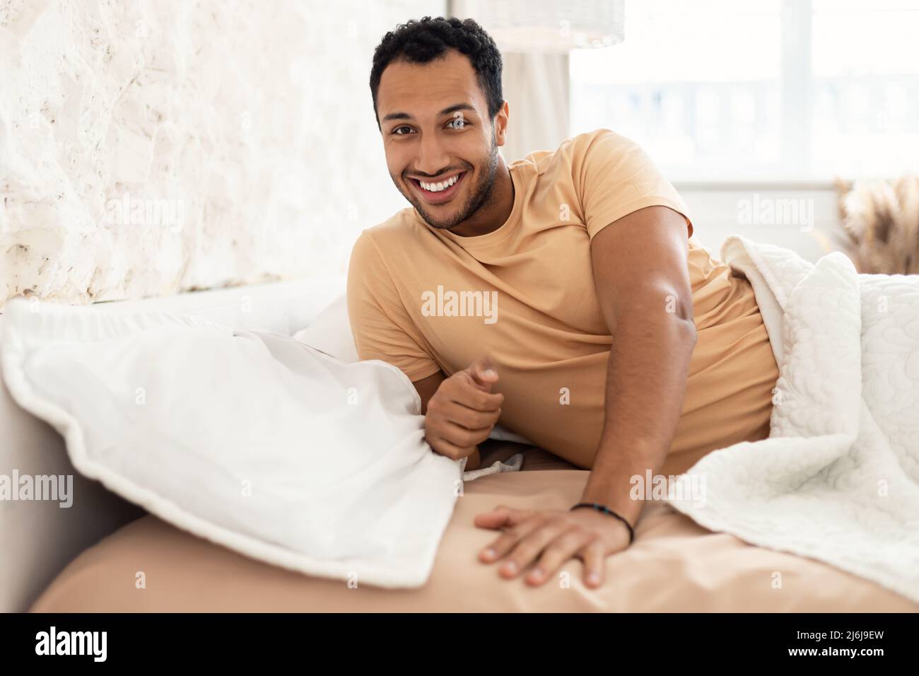 Gioioso uomo del Medio Oriente sorridente posando sdraiato nel letto all'interno Foto Stock
