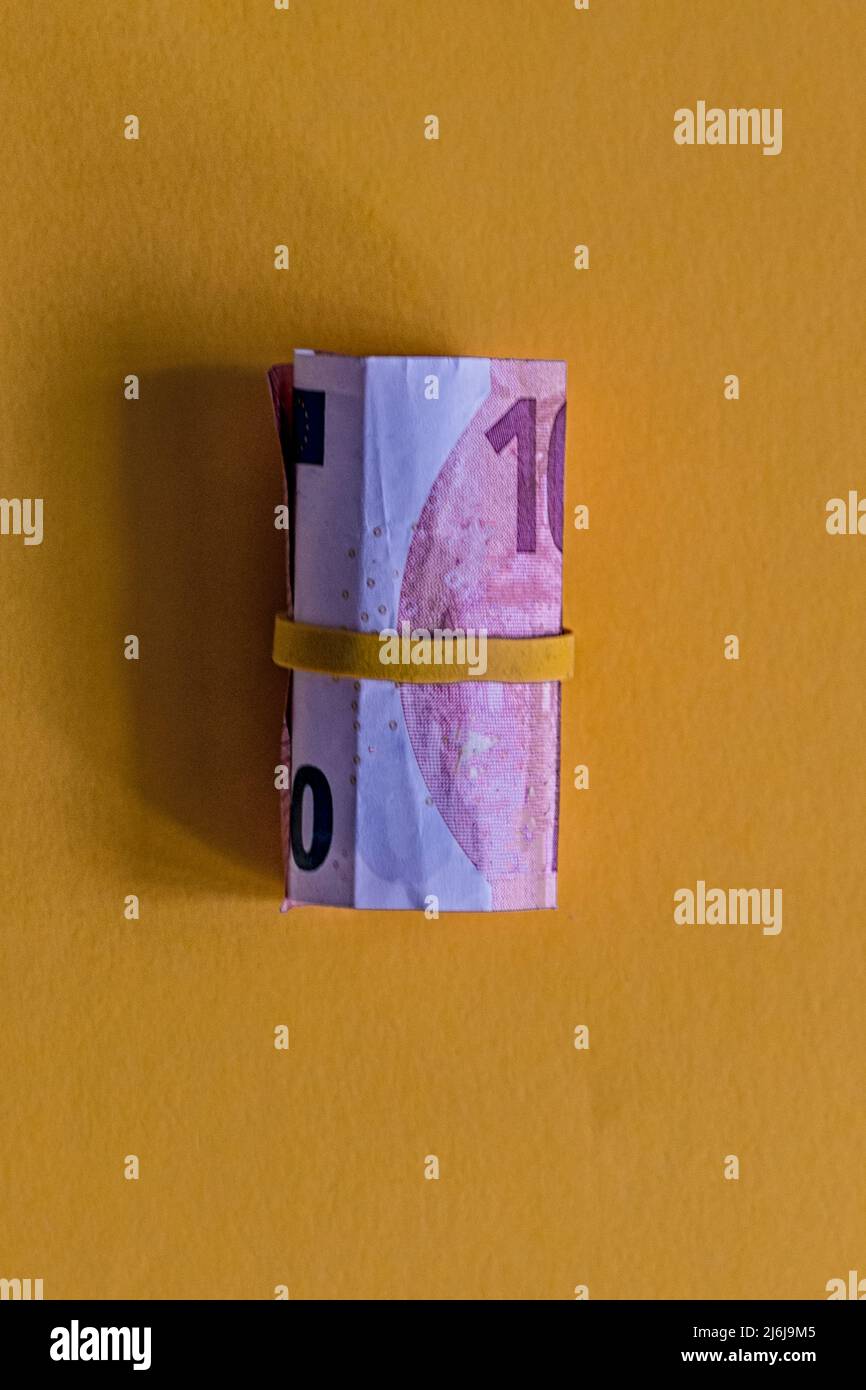 Grande borra di dieci banconote in euro con una fascia di gomma gialla su sfondo giallo. Foto Stock