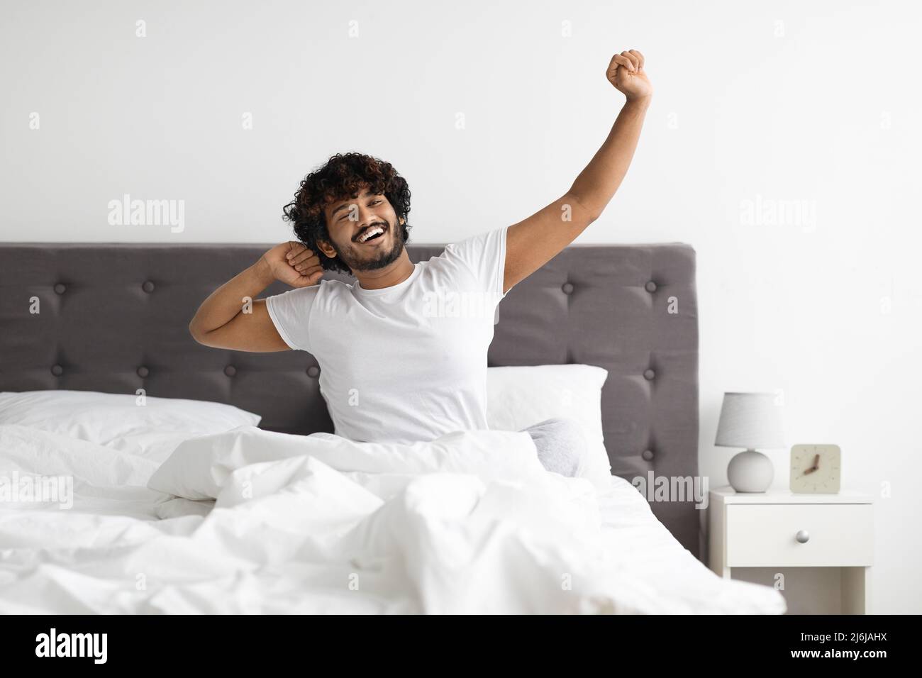 Ragazzo indiano ben riposato in pigiama che si allunga a a letto Foto Stock