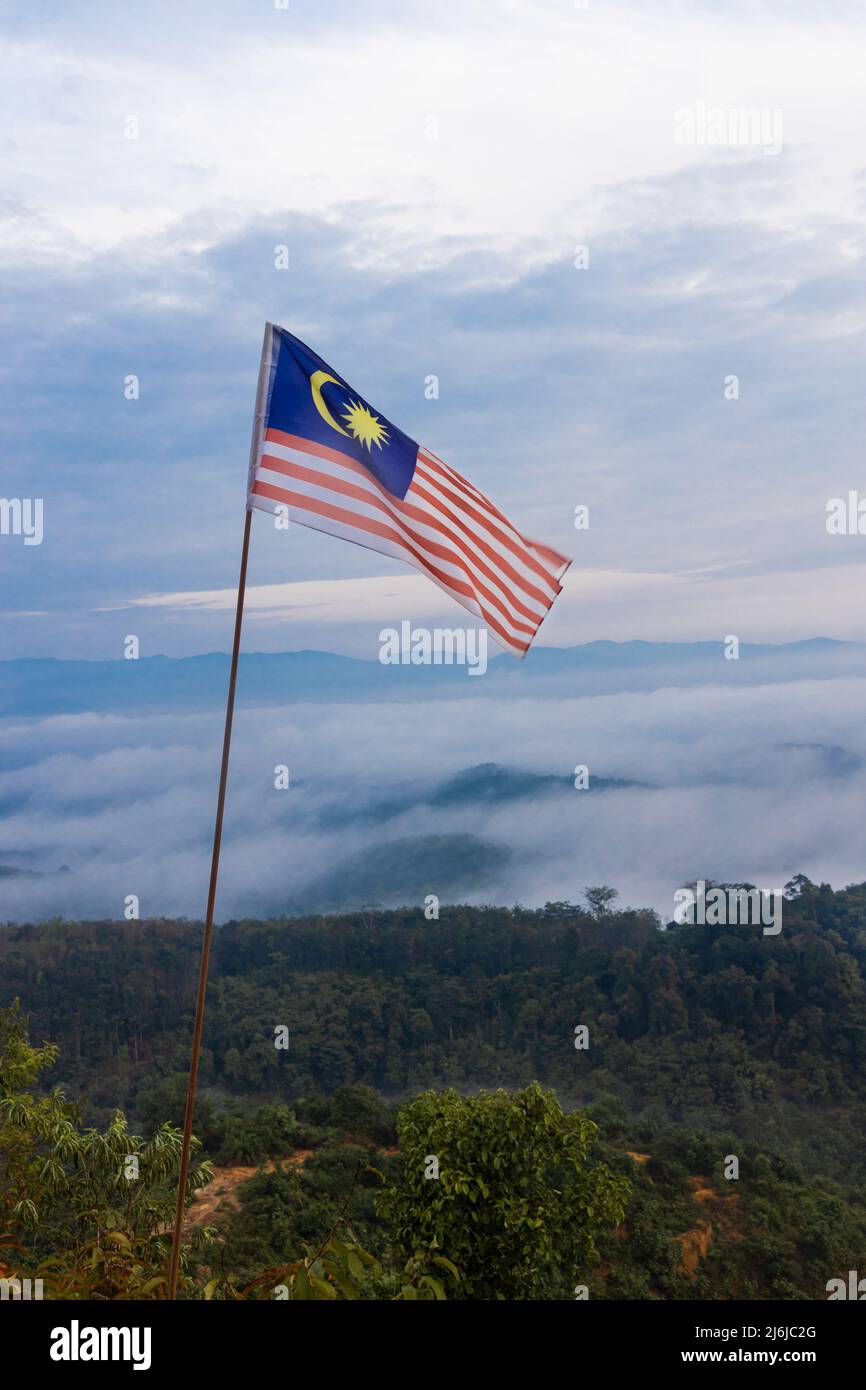 Bandiera della Malesia che vola in pole sull'altopiano di montagna contro il mare di nuvola e cielo blu Foto Stock