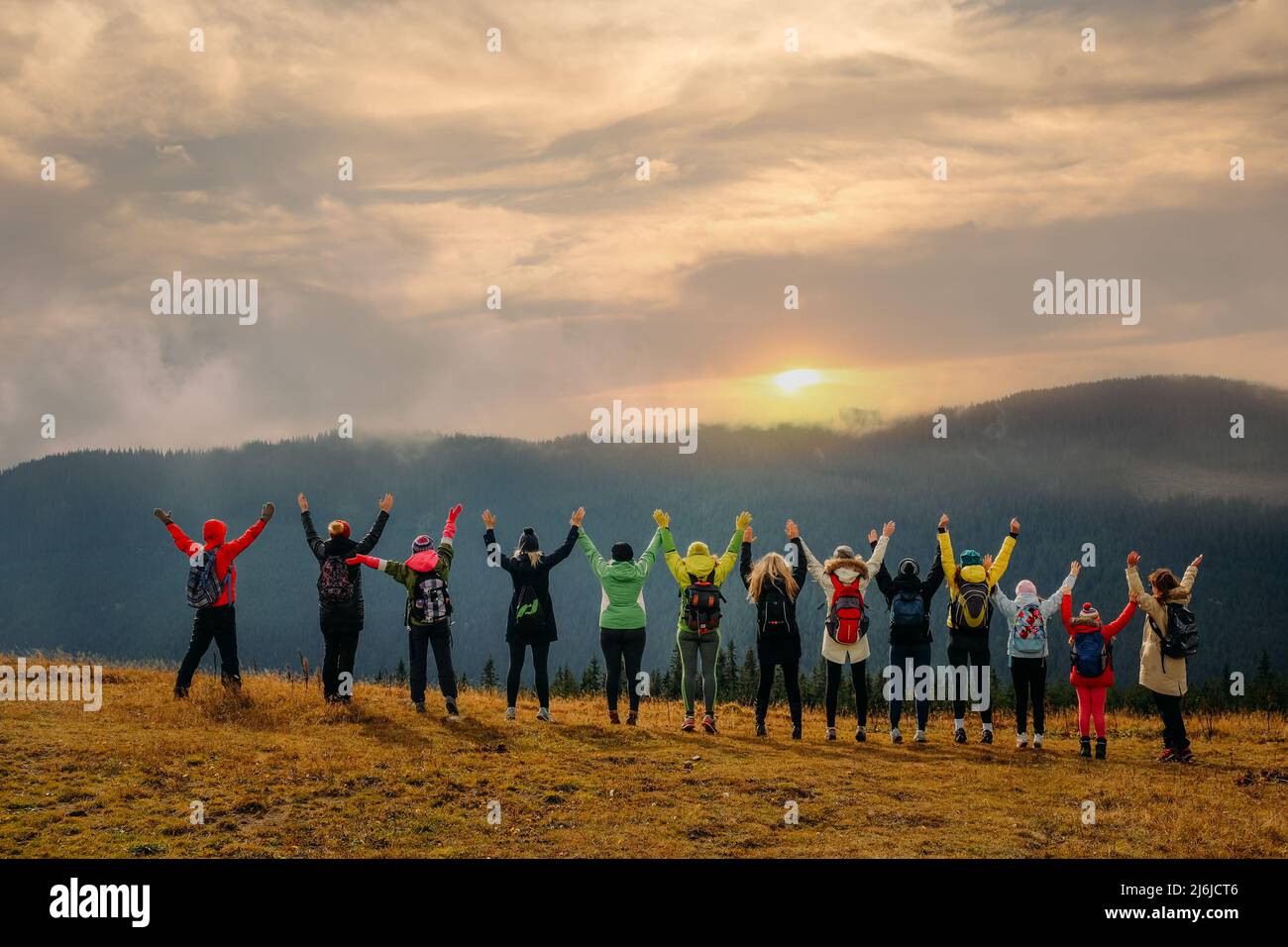 Un grande gruppo di amici viaggia insieme e goditi il paesaggio di montagna al tramonto con le mani rialzate Foto Stock