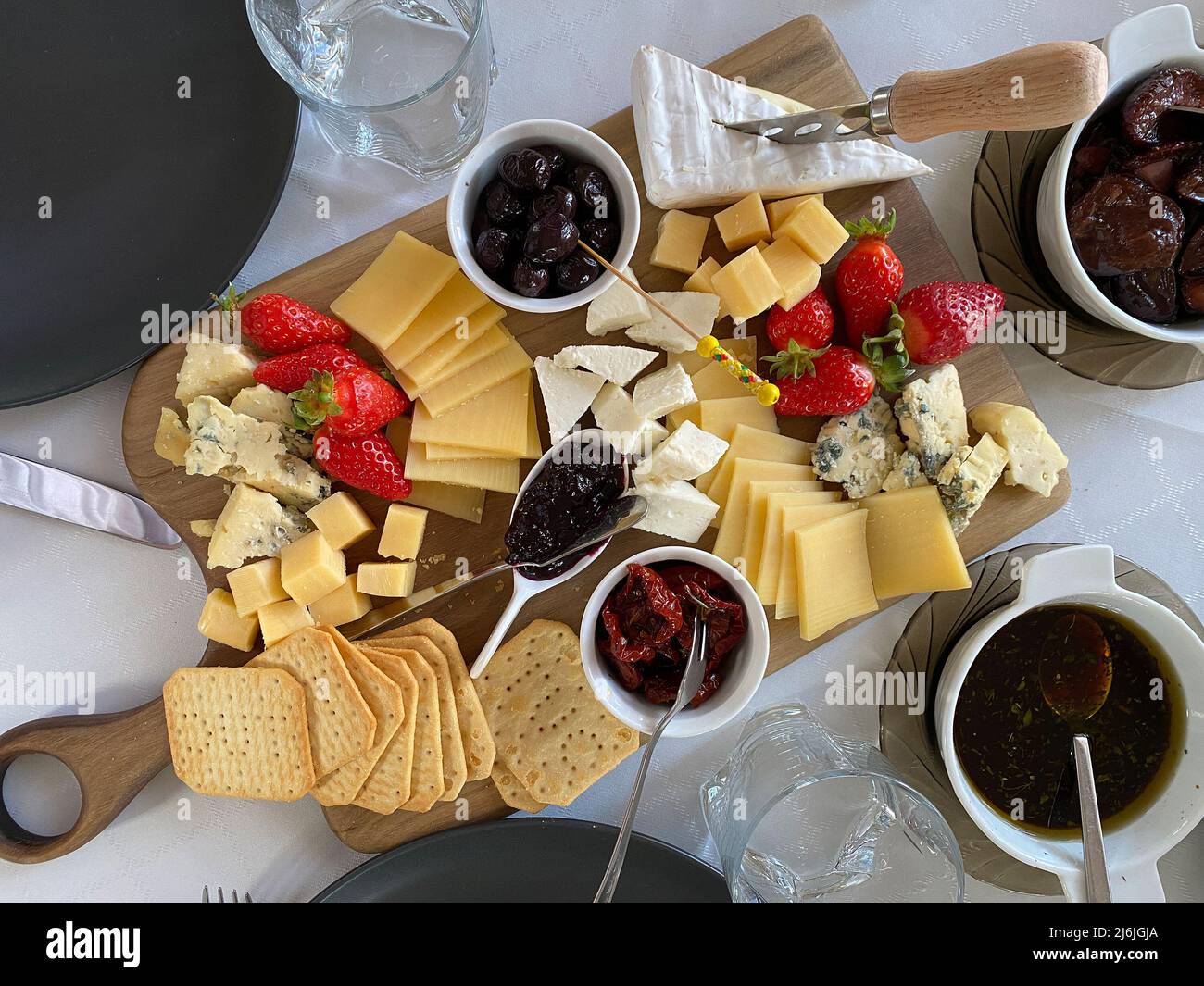 Piatto di formaggi con camembert, brie, dor blue, fragole, pomodori secchi, olive su un tavolo di legno, vista dall'alto. Foto Stock