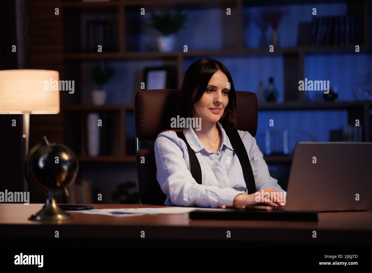 Giovane donna che lavora con un notebook in ufficio. Il lavoratore d'ufficio che analizza grafici e grafici, lavora in modo eccessivo mentre è seduto in ufficio fino a tardi. Cinematografico Foto Stock
