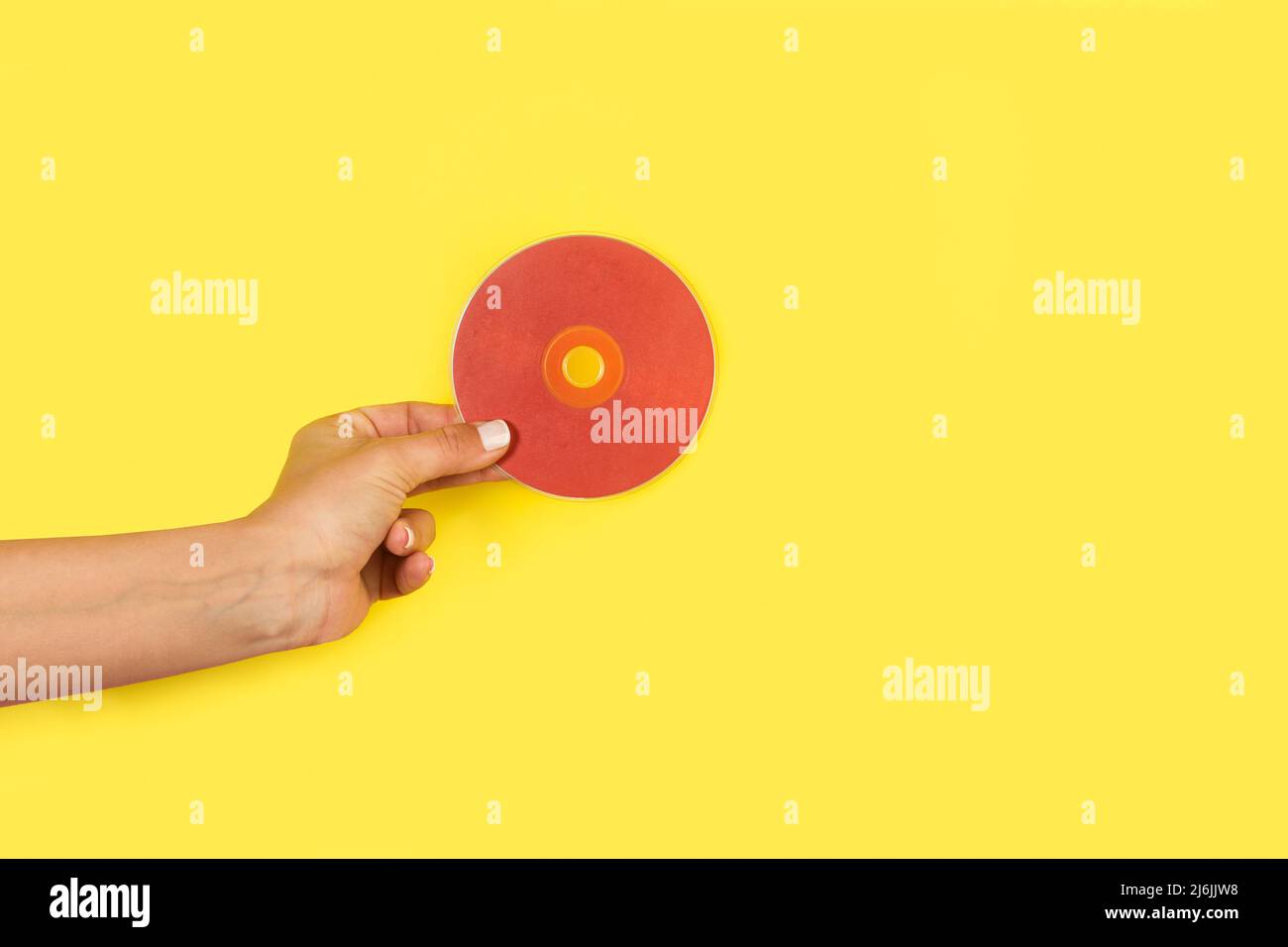 Mano donna che tiene un CD rosso su sfondo giallo con spazio per la copia Foto Stock