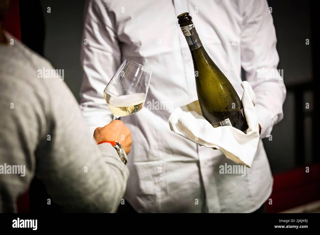 il cameriere con camicia bianca serve vino frizzante a un cliente, lavori e artigianato Foto Stock