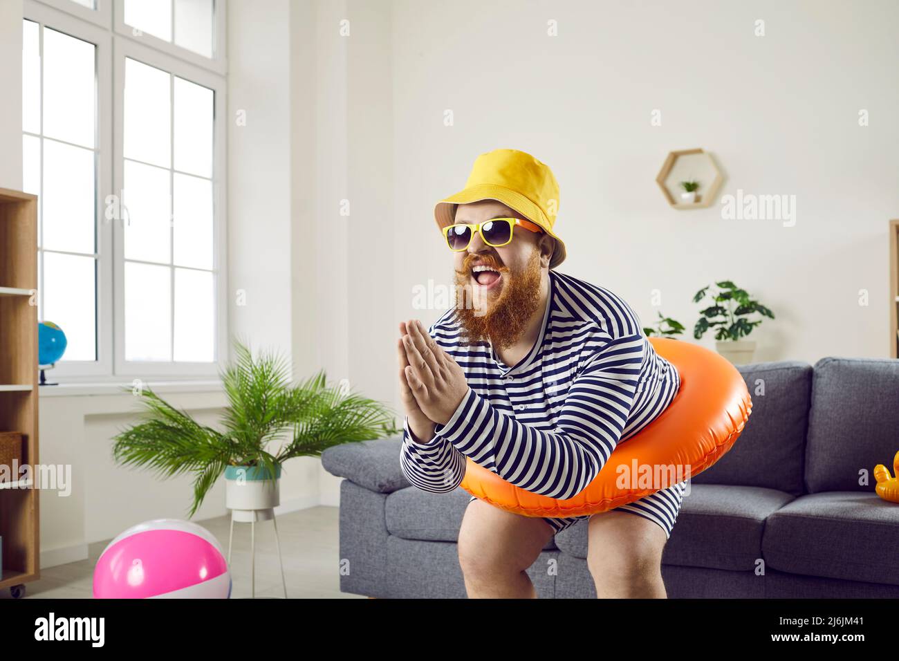 Divertente uomo pazzo con cerchio gonfiabile finge di nuotare a casa in soggiorno. Foto Stock
