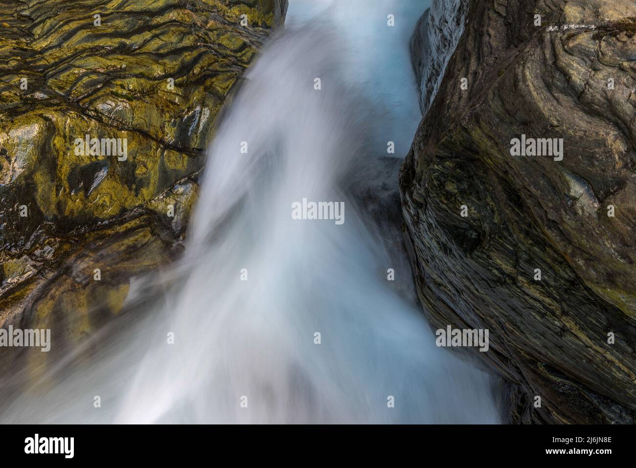 Tra le rocce cade un ruscello montano infestante di acqua limpida fotografata con la sfocatura del movimento. Foto Stock