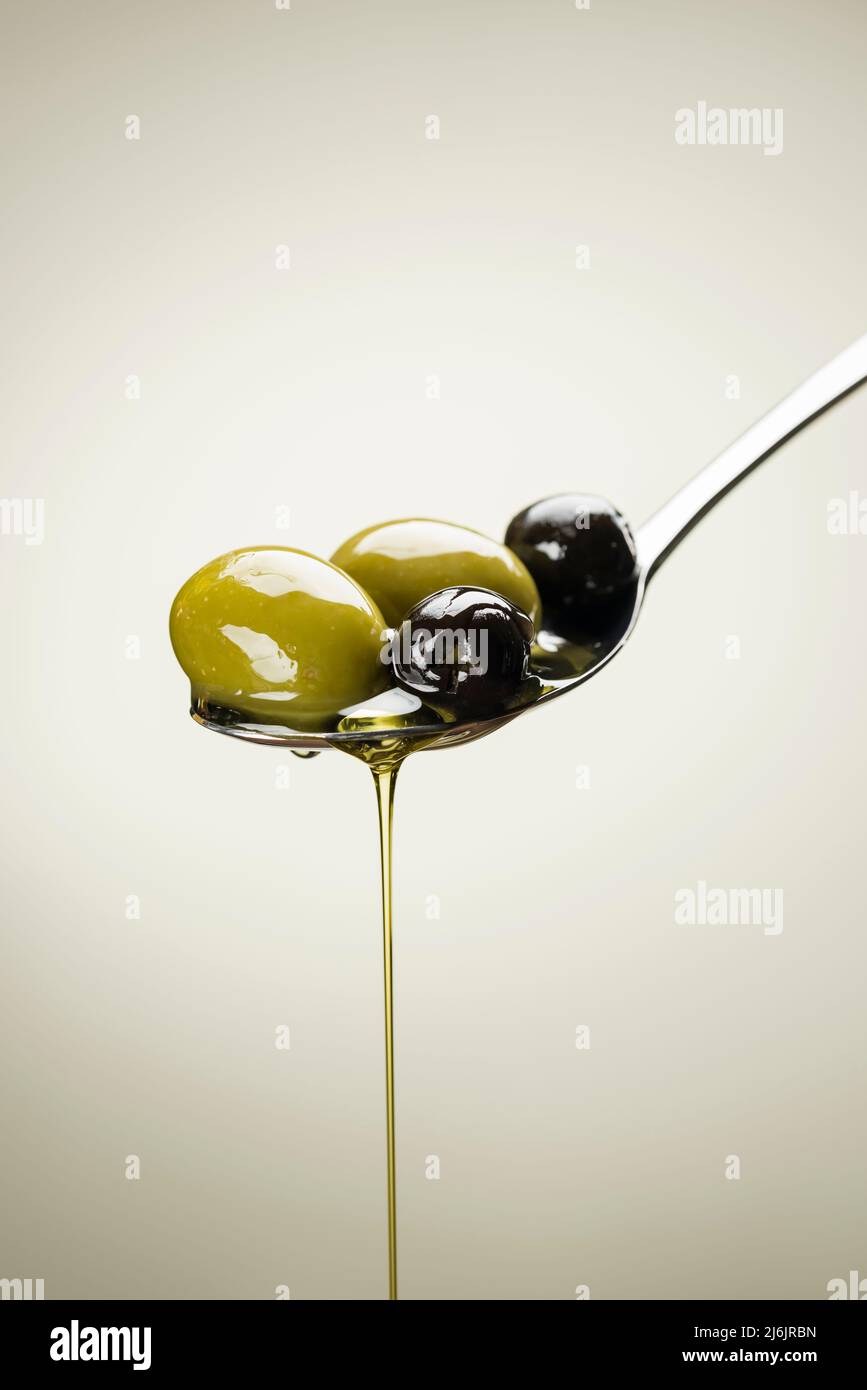 Grandi olive verdi e nere su un cucchiaio di olio gocciolante Foto Stock