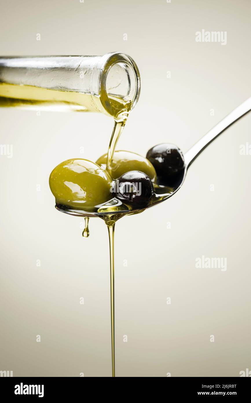Grandi olive verdi e nere su un cucchiaio di olio gocciolante Foto Stock