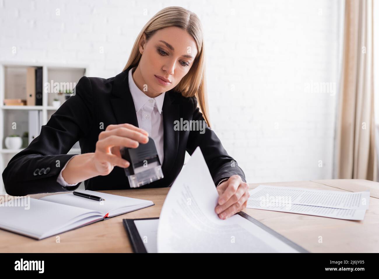 notaio biondo che tiene la timbratura mentre lavora con i documenti in ufficio Foto Stock