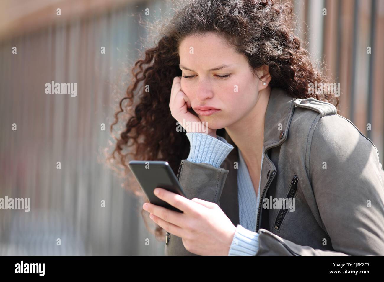 Annoiato donna che controlla smartphone seduto in strada Foto Stock