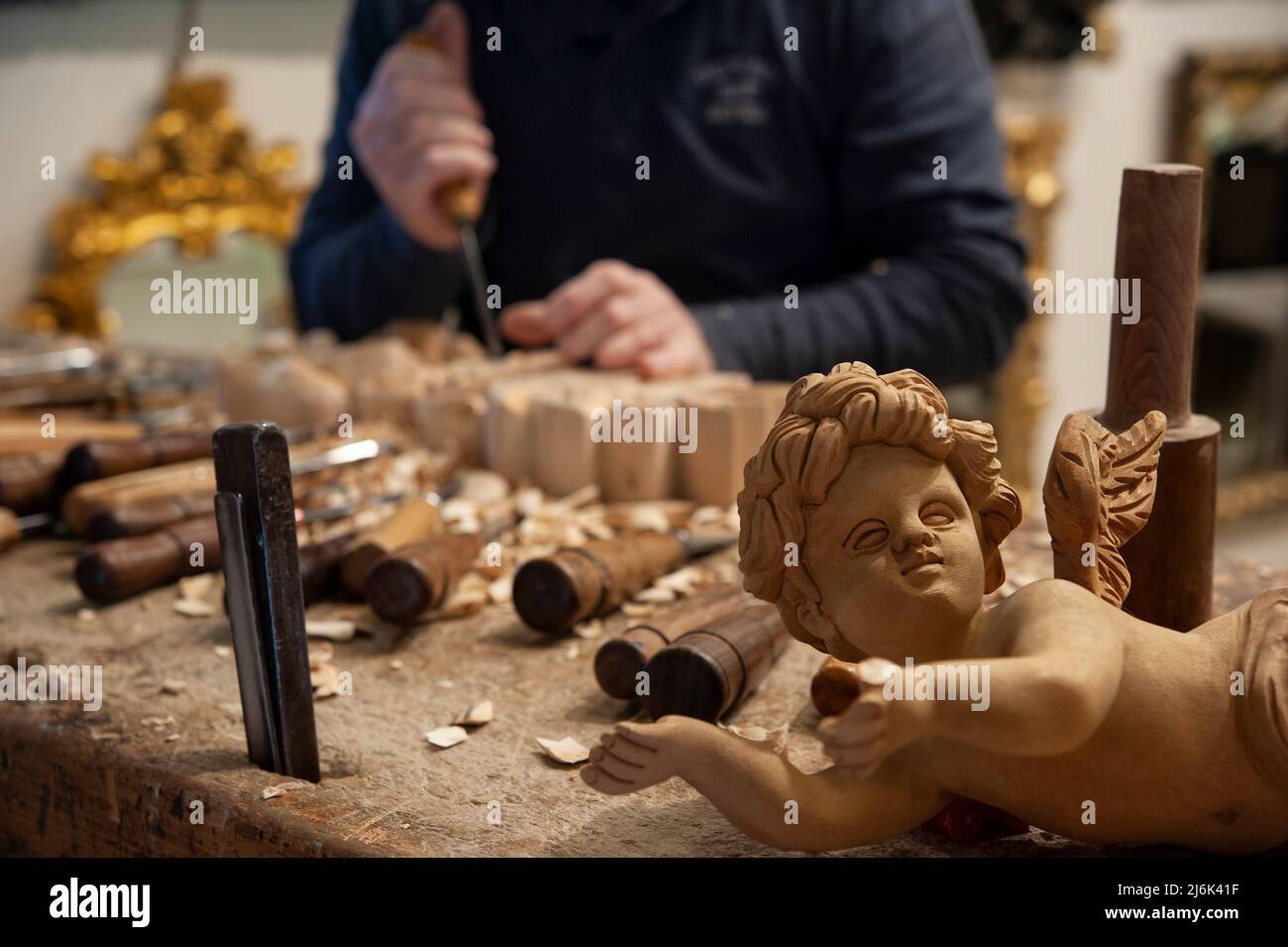 Maestro del legno al lavoro. Trucioli di legno, sgorbie e scalpelli sul banco di lavoro. Angelo legno intagliato in primo piano. Foto Stock