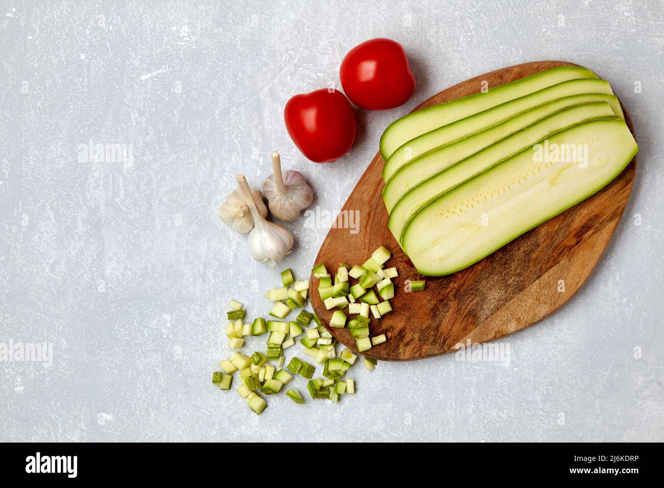 Verdure a fette con zucchine su un tagliere di legno, pomodori e aglio Foto Stock