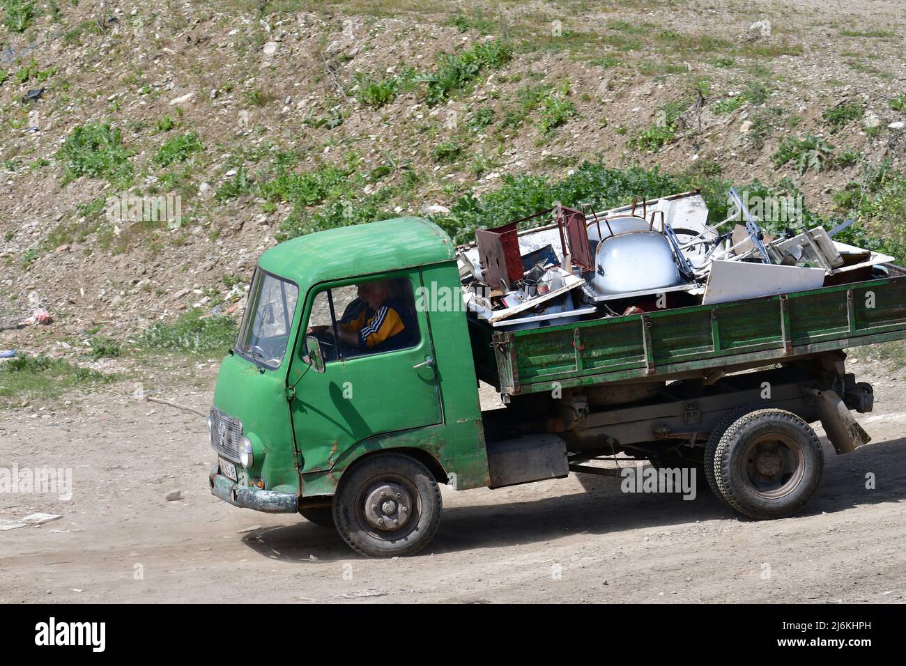Un piccolo camion con un rimorchio pieno di rottami metallici sta guidando su una strada macadam. Foto Stock