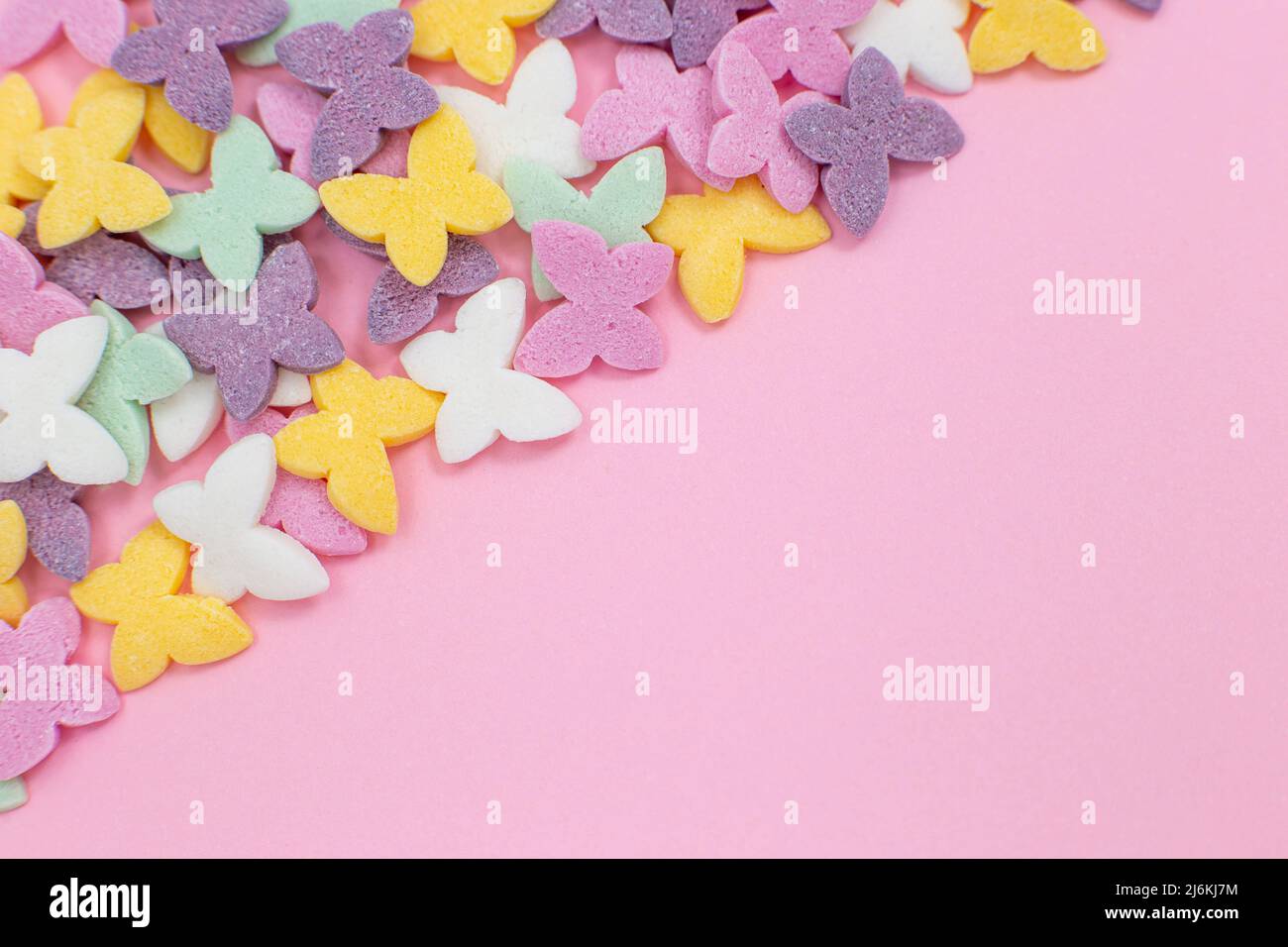 Le farfalle colorate, un popolare condimento a base di zucchero, giacciono su uno sfondo rosa diagonalmente nell'angolo sinistro. Foto Stock