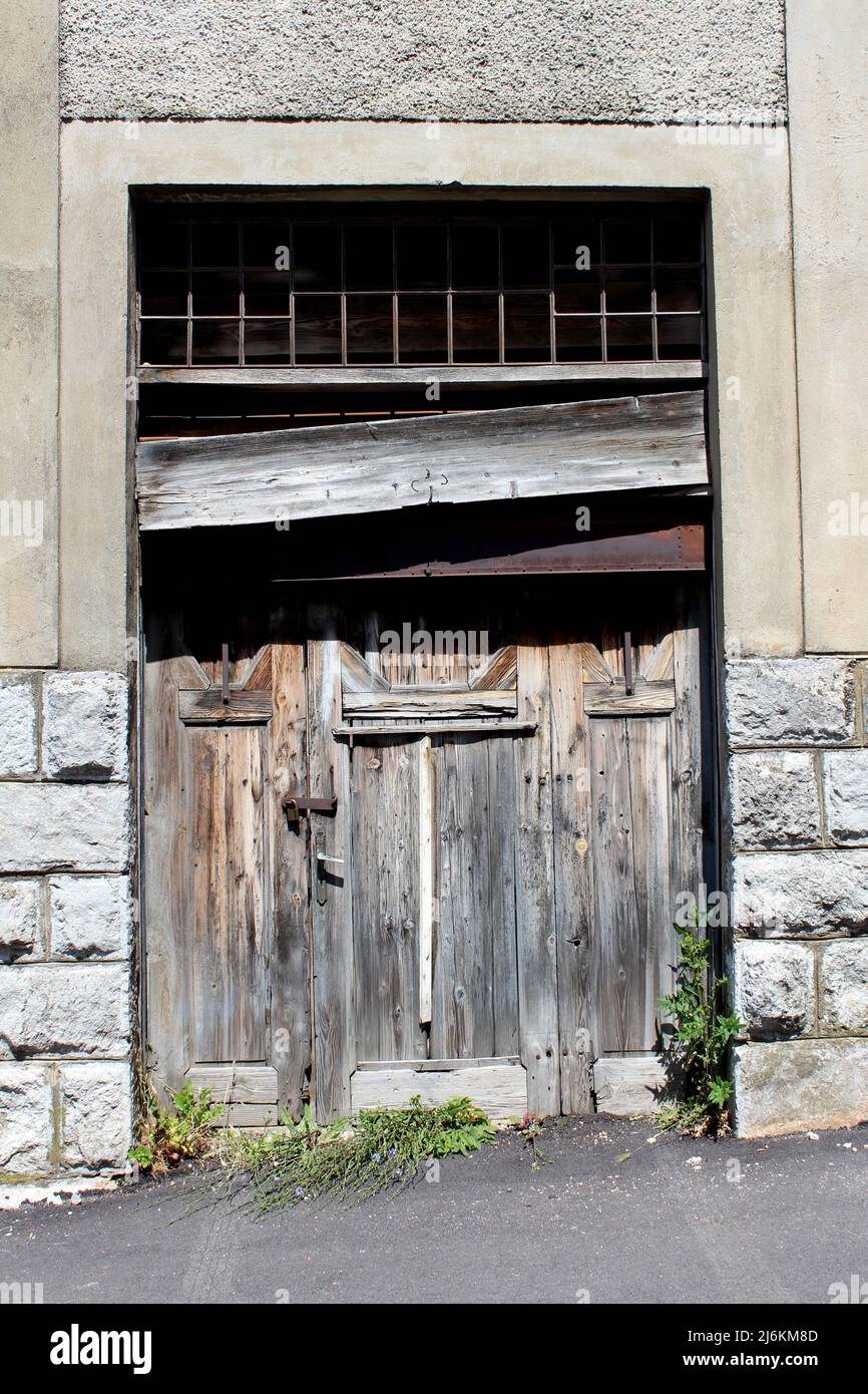 Grandi vecchie porte di ingresso in pannelli di legno fessurati dilapidati per la costruzione industriale abbandonata di fabbrica chiusa con lucchetto arrugginito coperto di legno Foto Stock