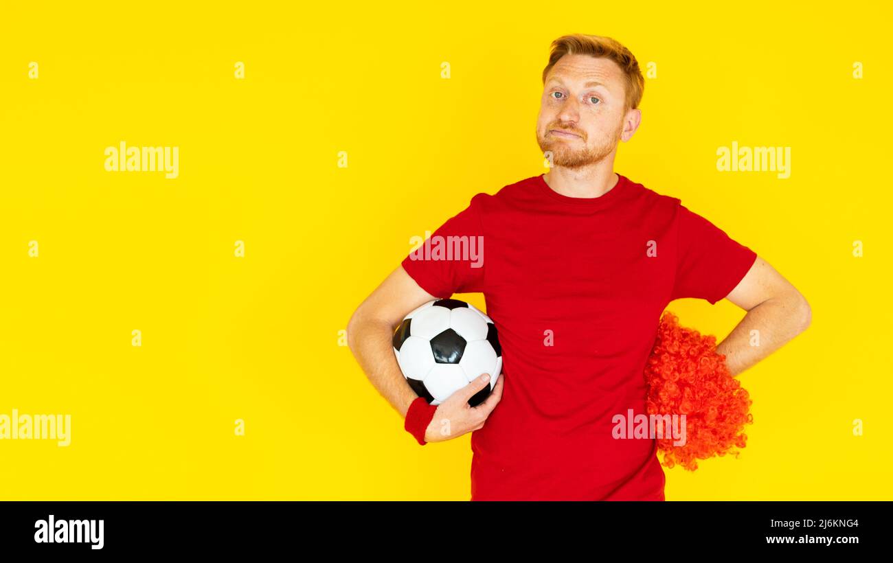 Un tifoso che sostiene una palla da calcio su sfondo giallo Foto Stock