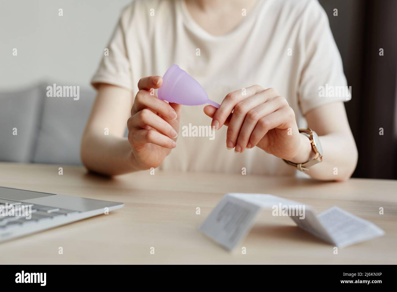 Primo piano minimo della giovane donna che tiene la tazza mestruale con il manuale di istruzioni in primo piano, spazio copia Foto Stock