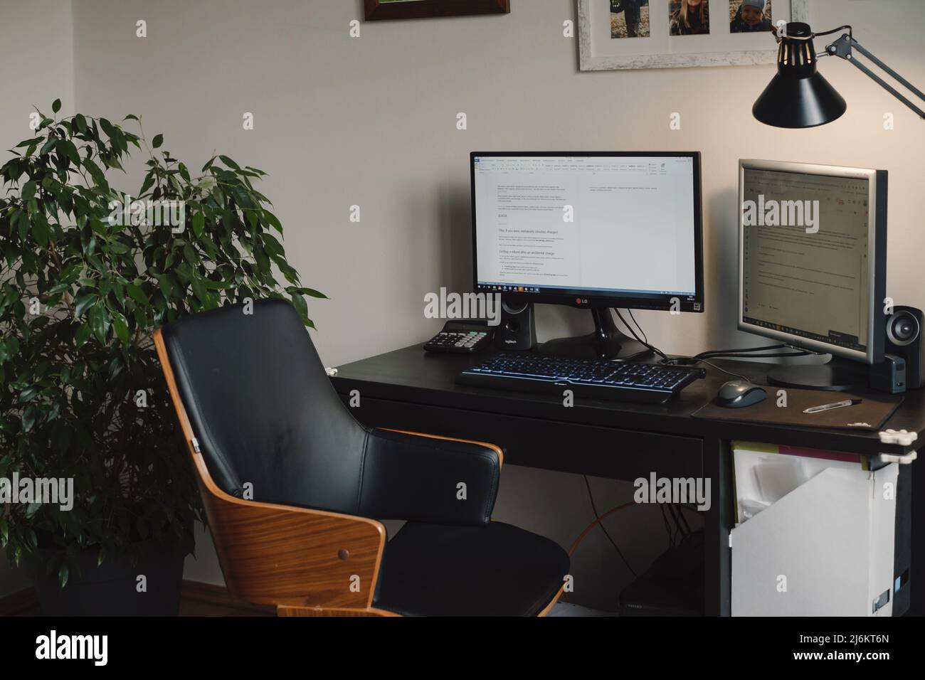 Spazio di lavoro per freelance, ambiente di lavoro domestico con computer e schermo. Scrivania confortevole senza persone con impianto e lampada. Sedia Boho vintage da Foto Stock