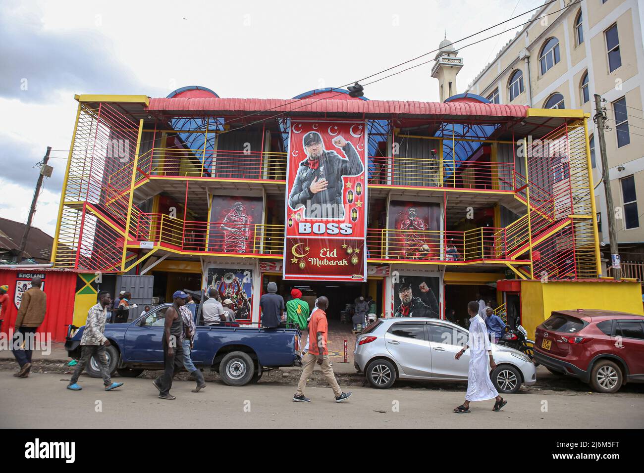 Kenyans camminano oltre un grande banner con il ritratto del direttore di Liverpool Jürgen Klopp che desidera mussulmani un felice Eid al complesso di shopping Anfield lungo la strada di Digo a Majengo. I musulmani in Kenya celebrano Eid-UL-Fitr che segna la fine del mese Santo del Ramadhan. Foto Stock