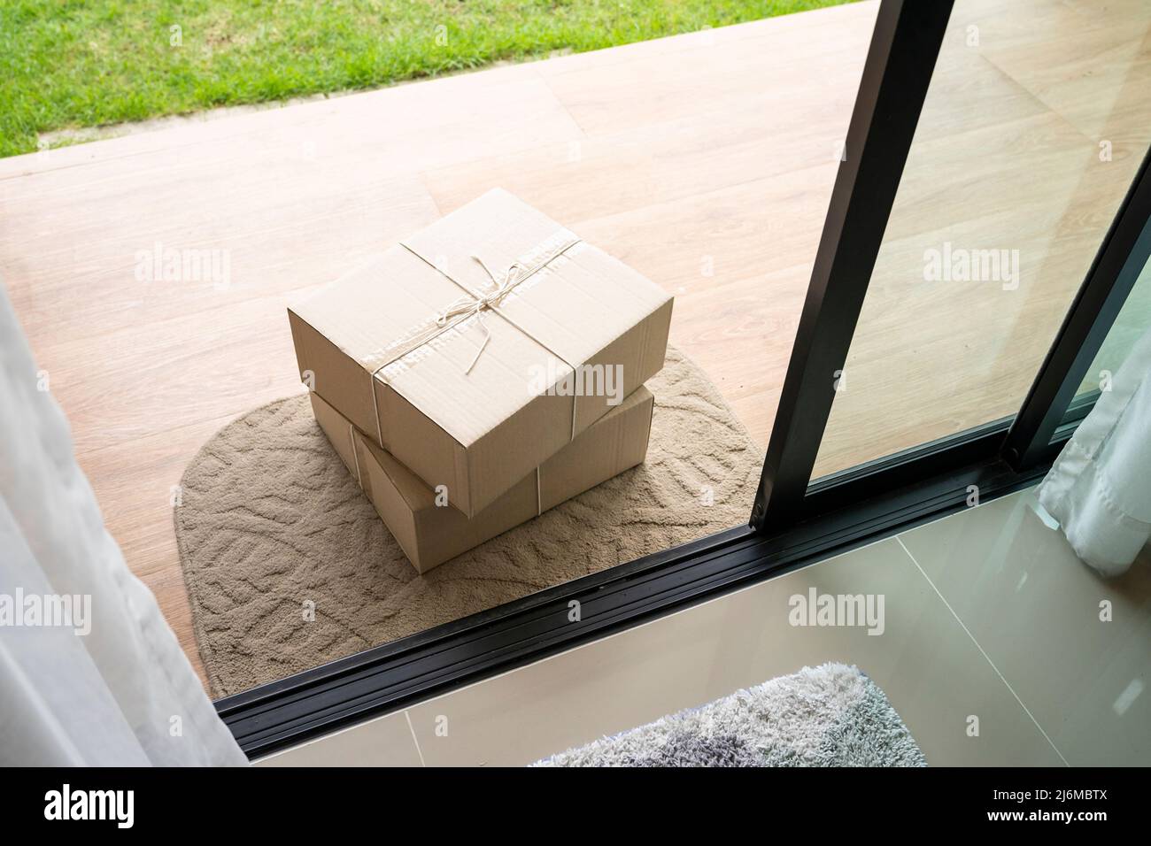 Consegnare la scatola dei pacchi sul tappetino dello sportello vicino alla porta di ingresso Foto Stock