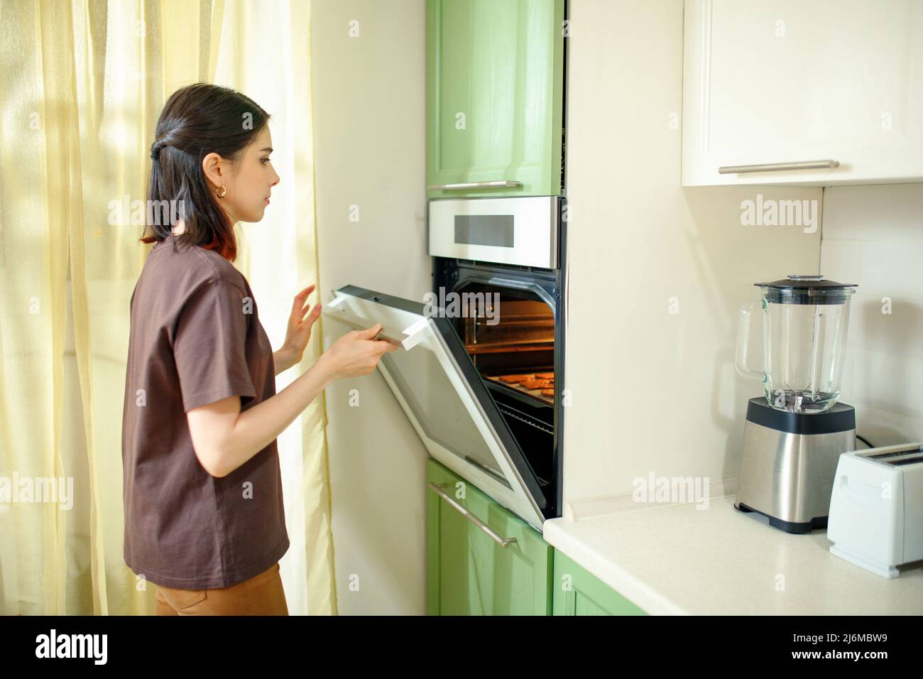Giovane donna brunetta che prepara torte fatte in casa in un moderno forno a muro. Foto Stock