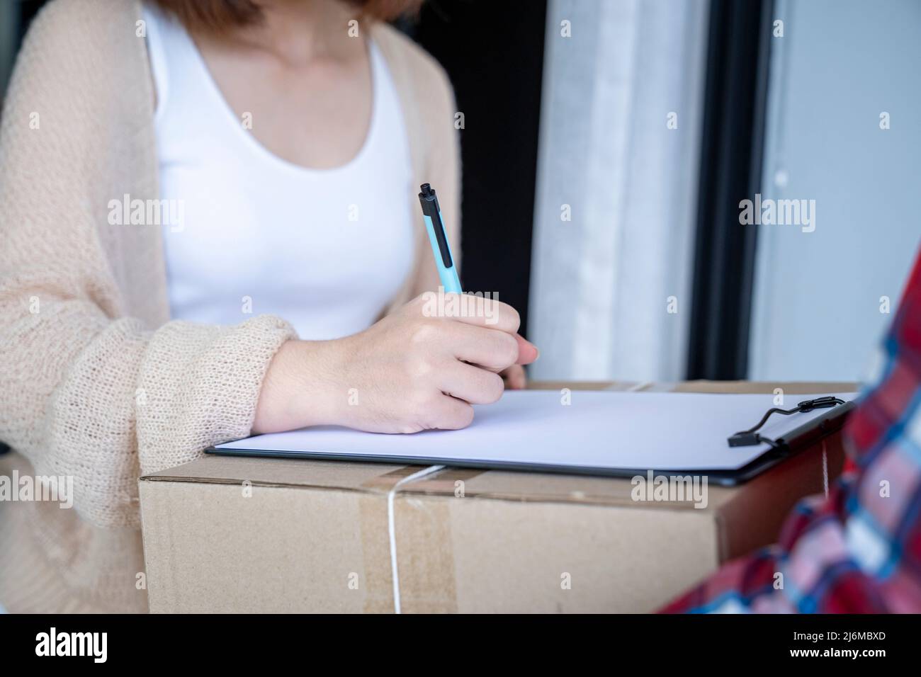 Donna firma i documenti mentre riceve pacchi dal corriere. Concetto di shopping online per consegna e ordine. Foto Stock